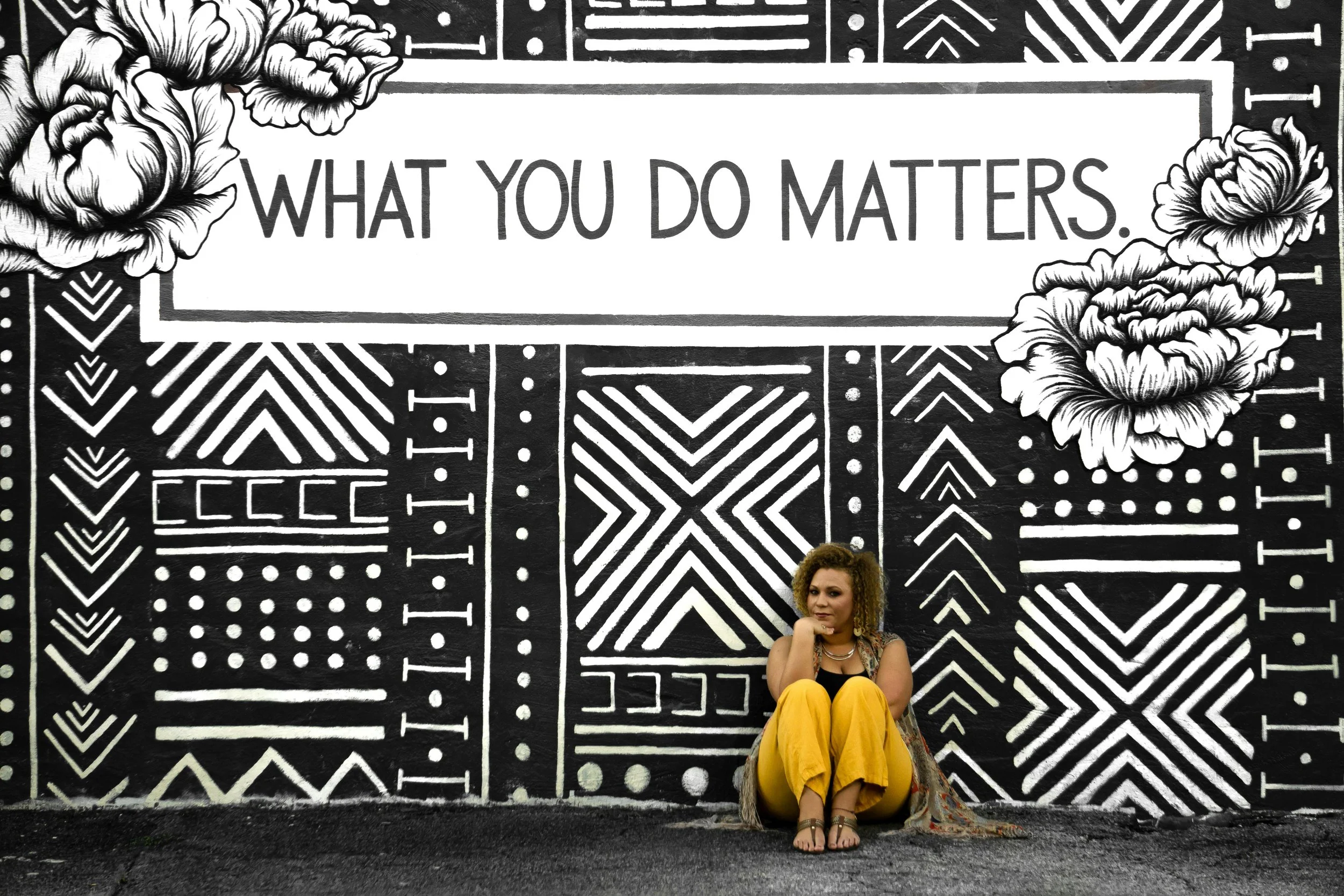 A woman sits in front of a mural in Birmingham, Alabama. The mural is black and white, and reads: "What you do matters"