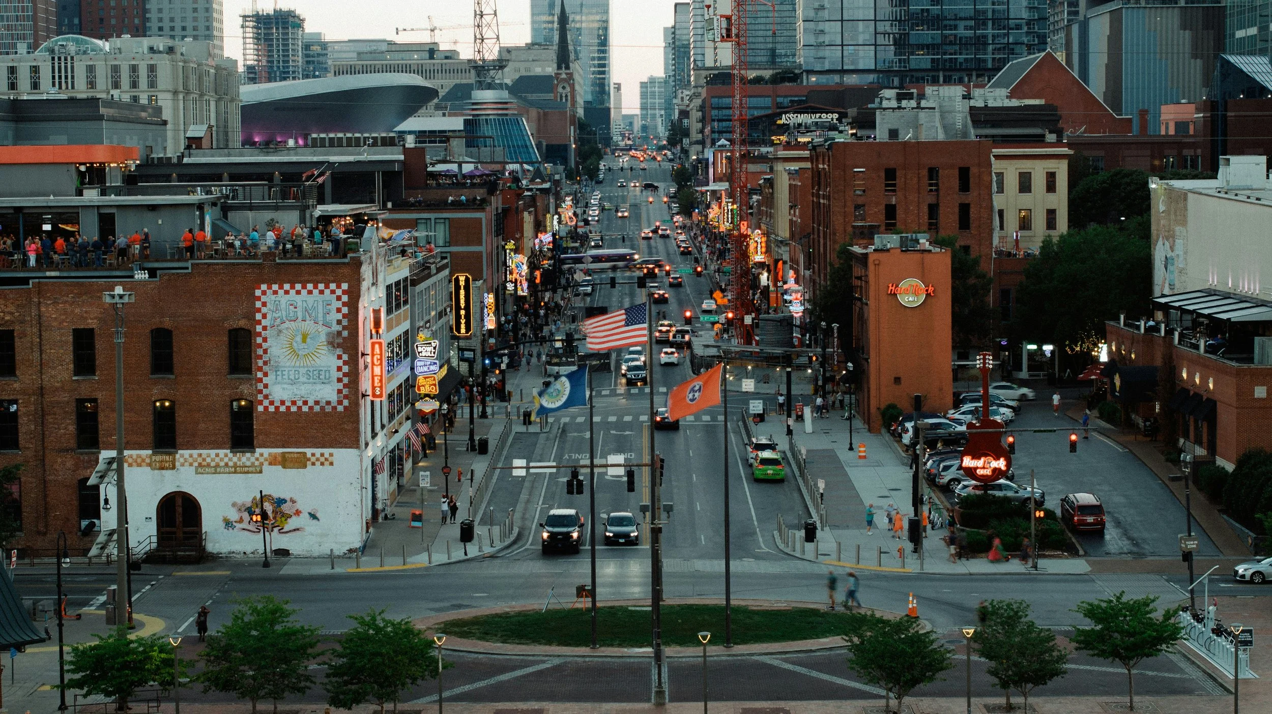 Broadway in Nashville, Tennessee. An American flag flies above the street which is full of people and bars. Drives & Detours Nashville self-guided tour