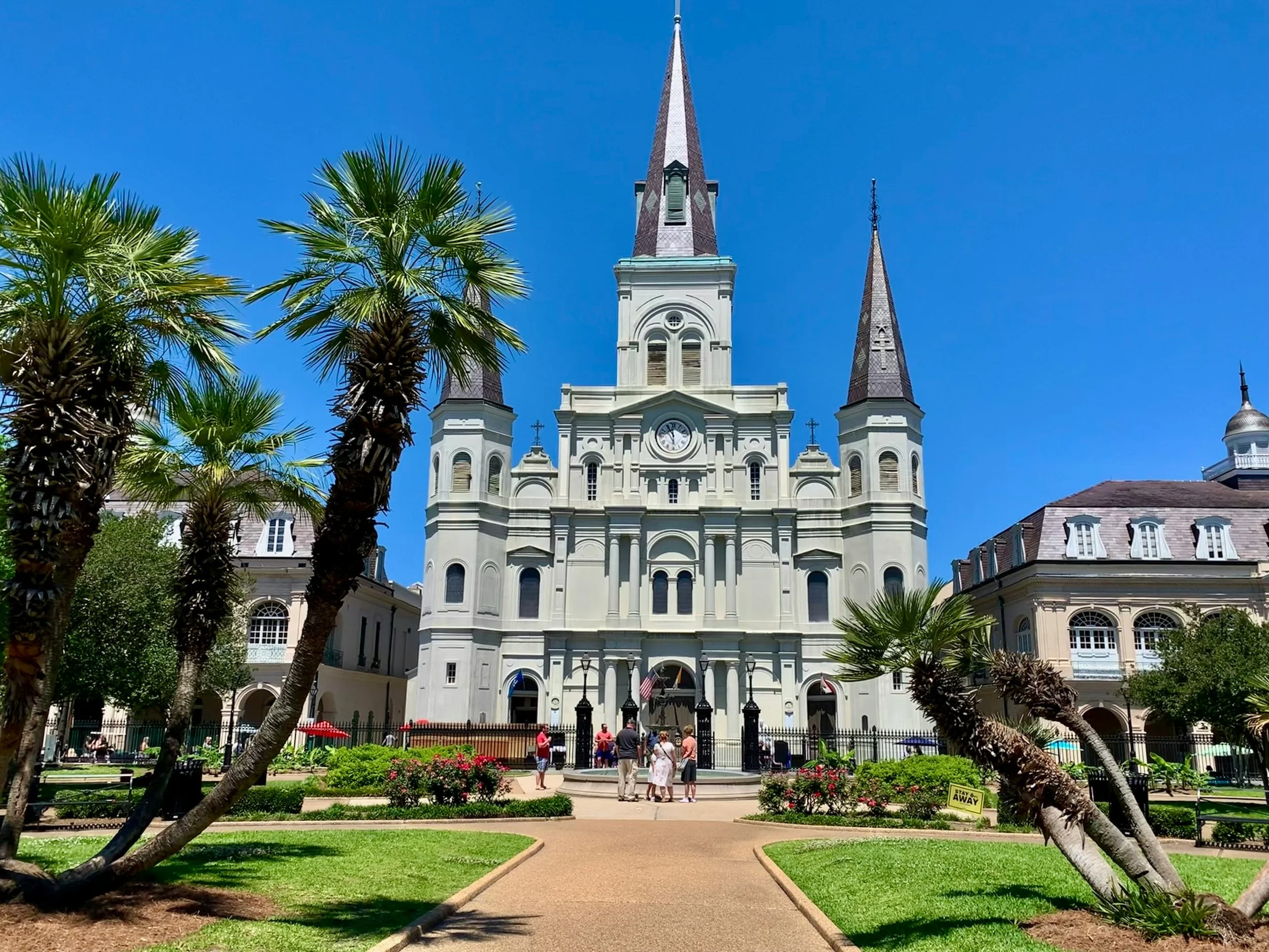St. Louis Cathedral towers over the manicured Jackson Square. People look up at the buiolding with three spires. Drives & Detours New Orleans walking tour