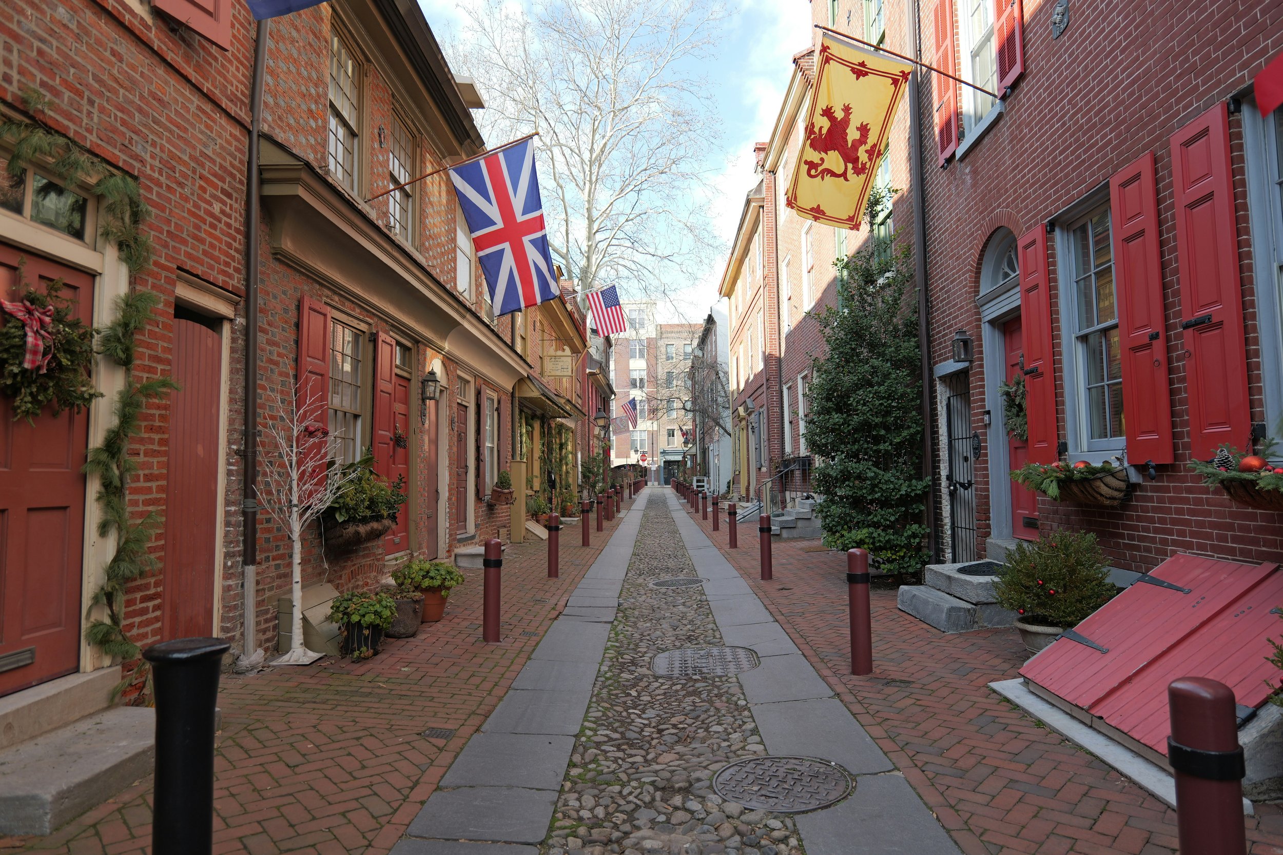 Elfreth’s Alley, Philadelphia, is a small cobbled street lined with small houses flying American flags, and a Union Jack. It's very narow and lined with bollards