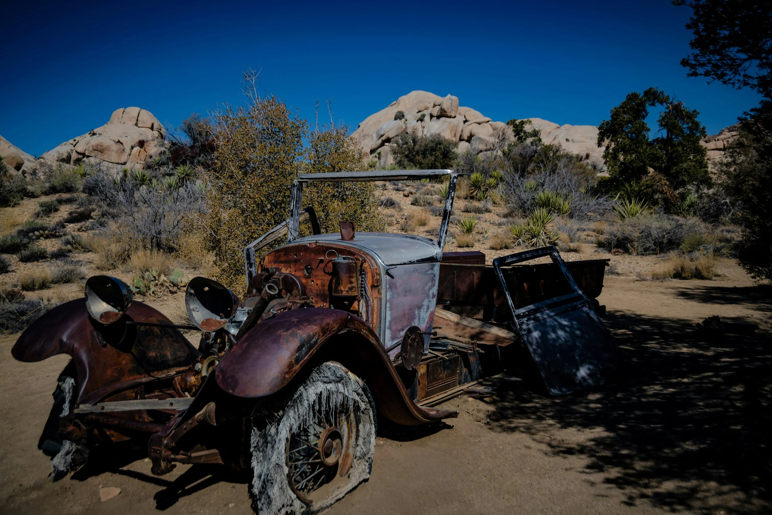 A rusted classic car, full of bullet holes, at Wall Street Mill. Drives & Detours Joshua Tree Audio Tour