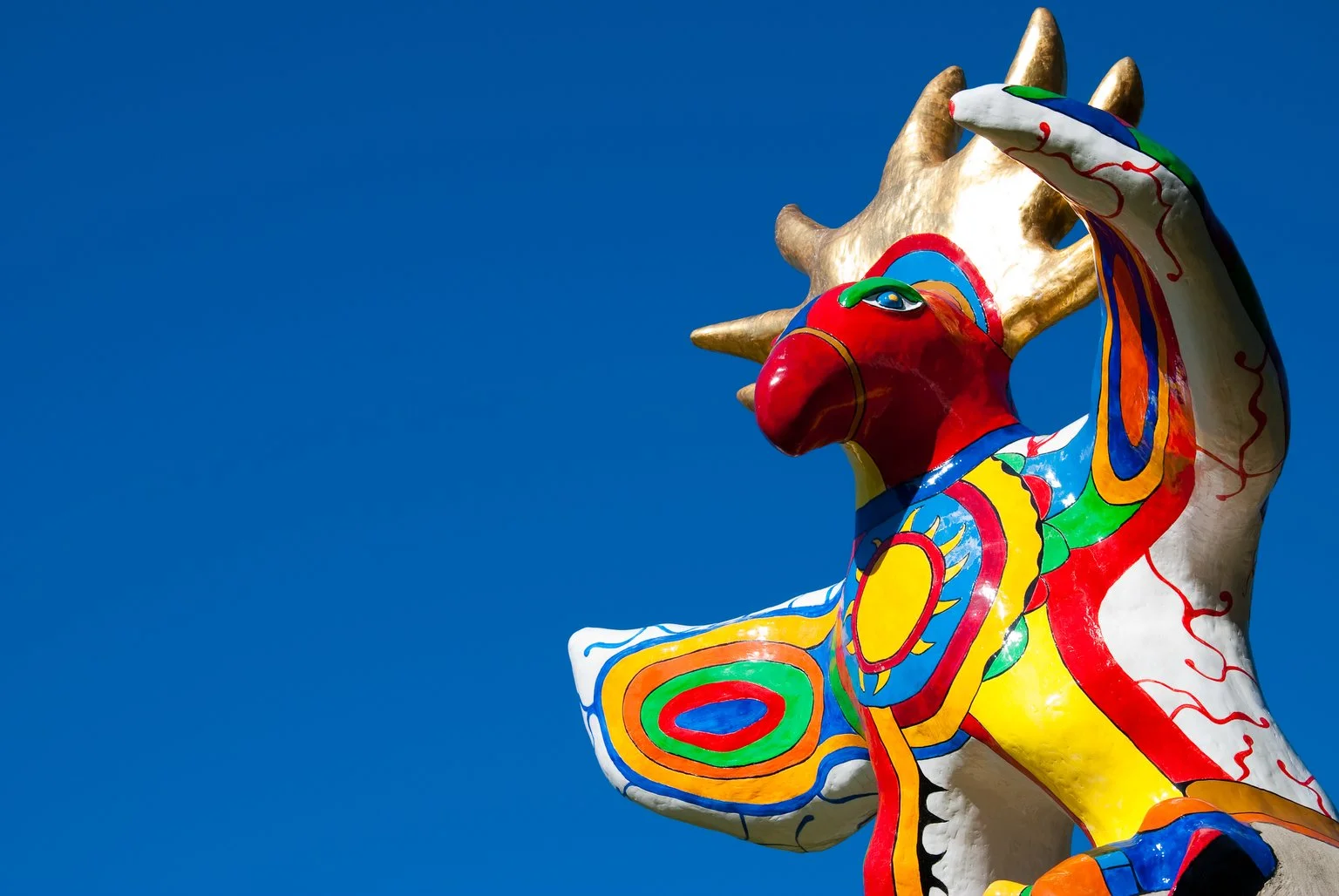 Sun God by Niki de Saint Phalle is a vibrant sculpture of a bird with its wings spread. It wears a crown like the sun, and has a sun on its chest