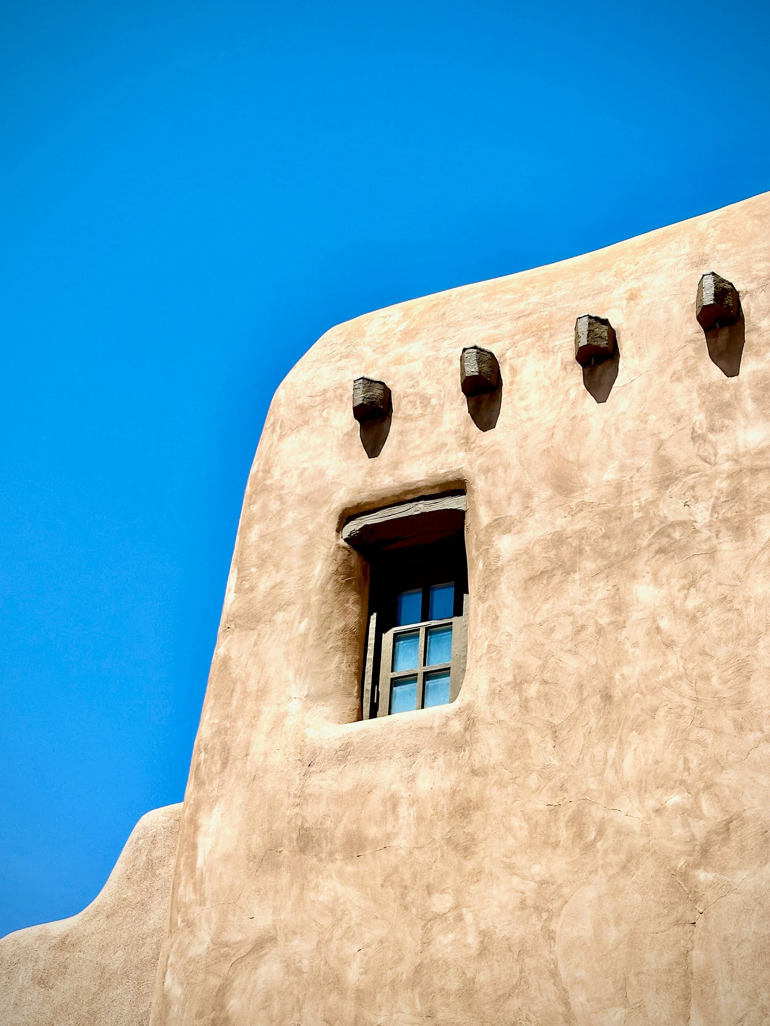 A window of an adobe building in Santa Fe reflects the blue sky