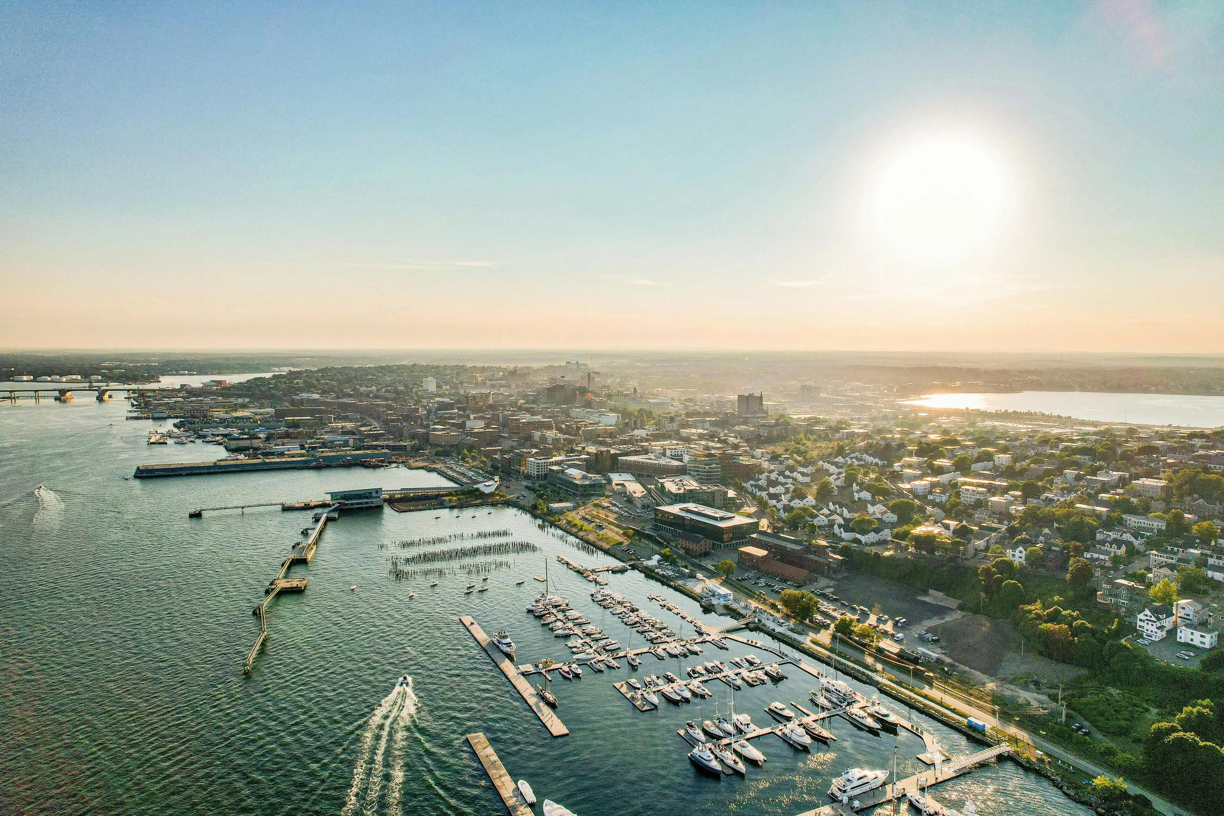 An aerial view of Portland, Maine. The sun is low in the sky and small boats are entering and leaving the port