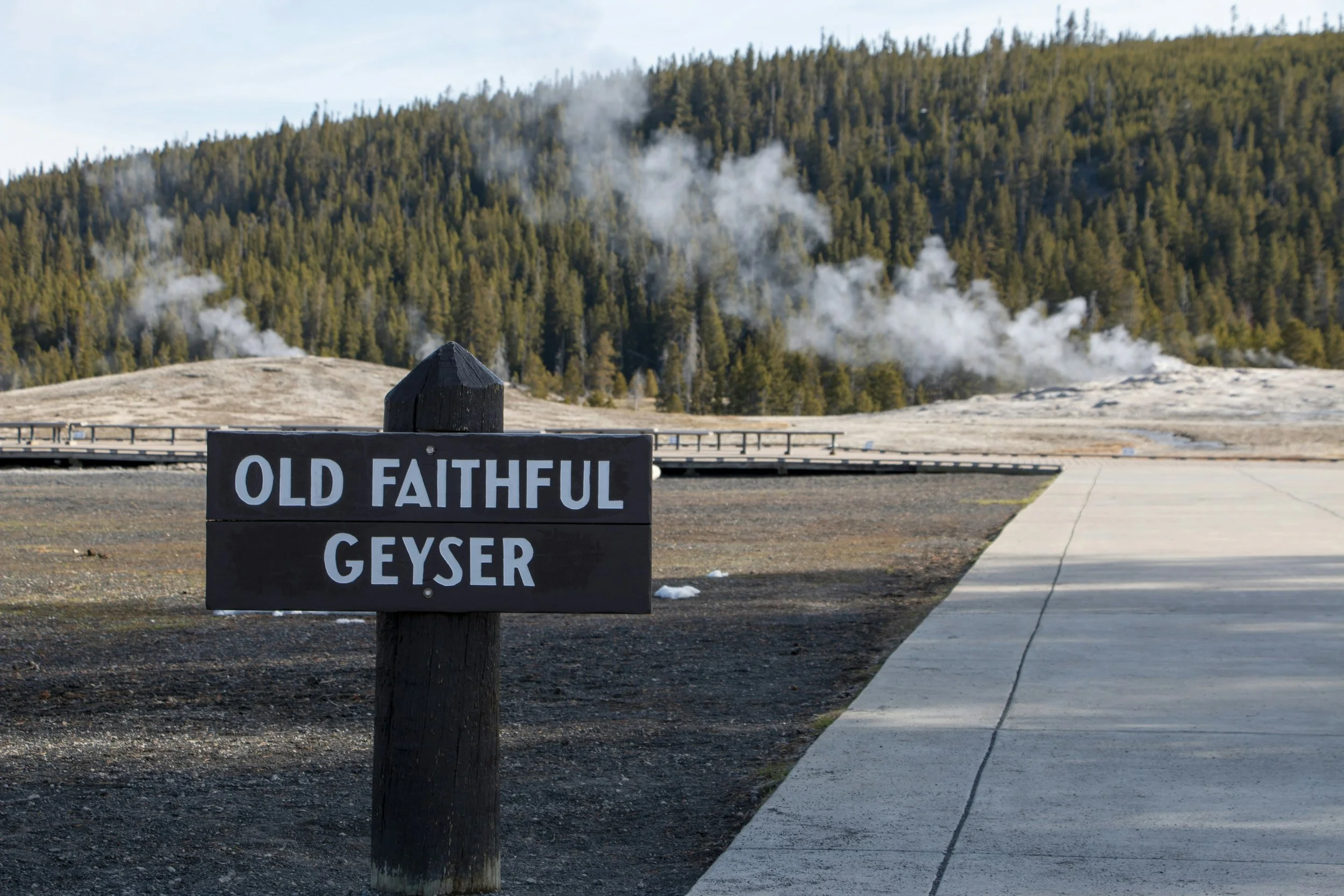 Steam rises behind a wooden sign that reads: Old Faithful Geyser. Drives & Detours Yellowstone National Park top sights
