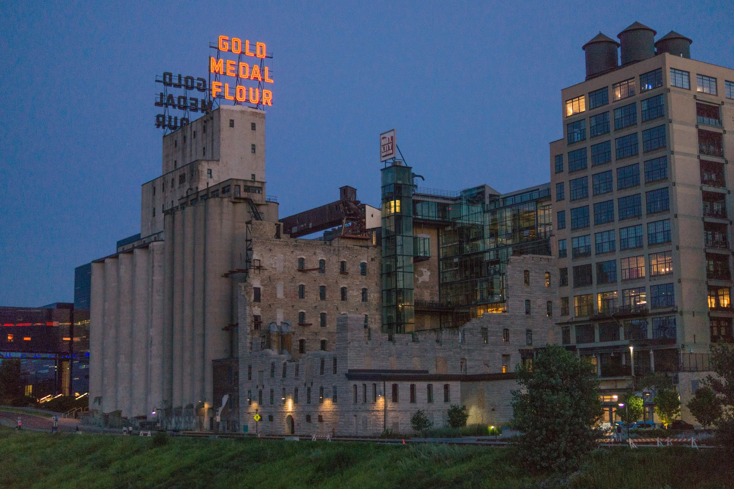 The Gold Medal Flour sign is lit up at dusk over an old factory in Mill City. Drives & Detours Minneapolis self-guided tour