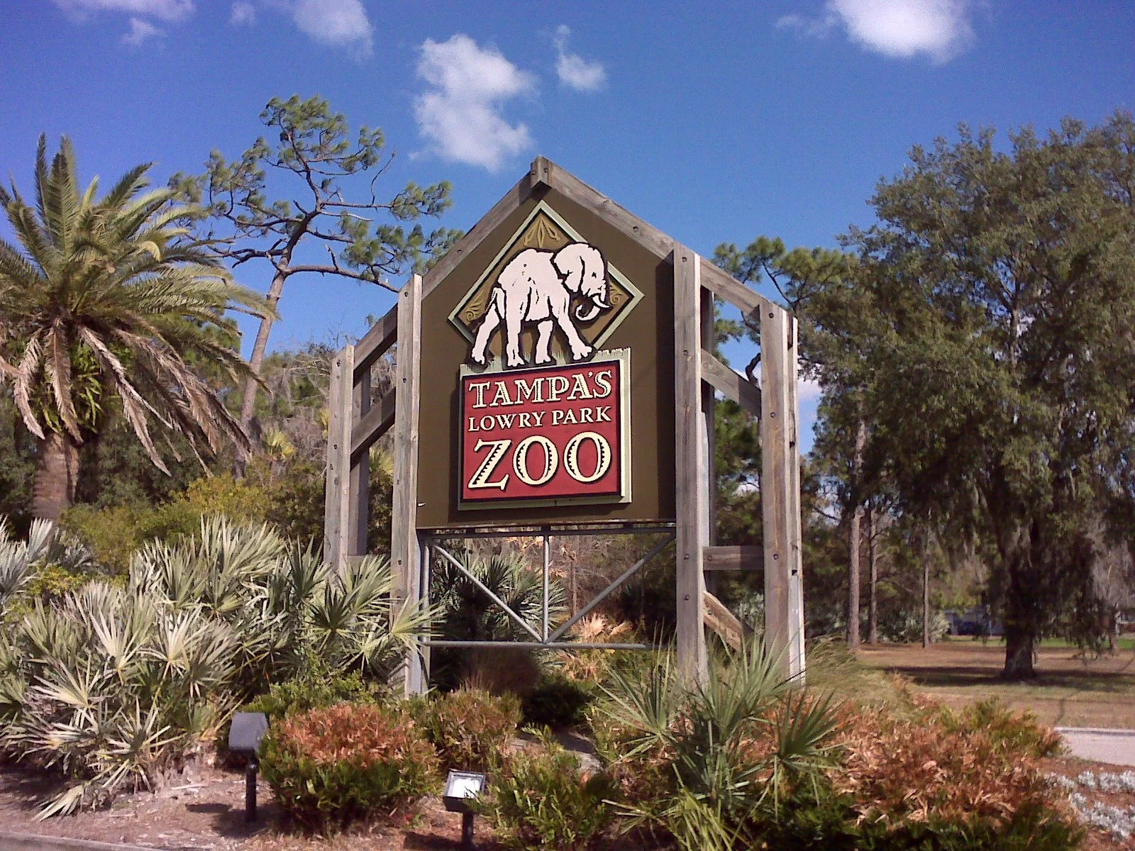 A sign for ZooTampa at Lowry Park surrounded by palm trees and brush.