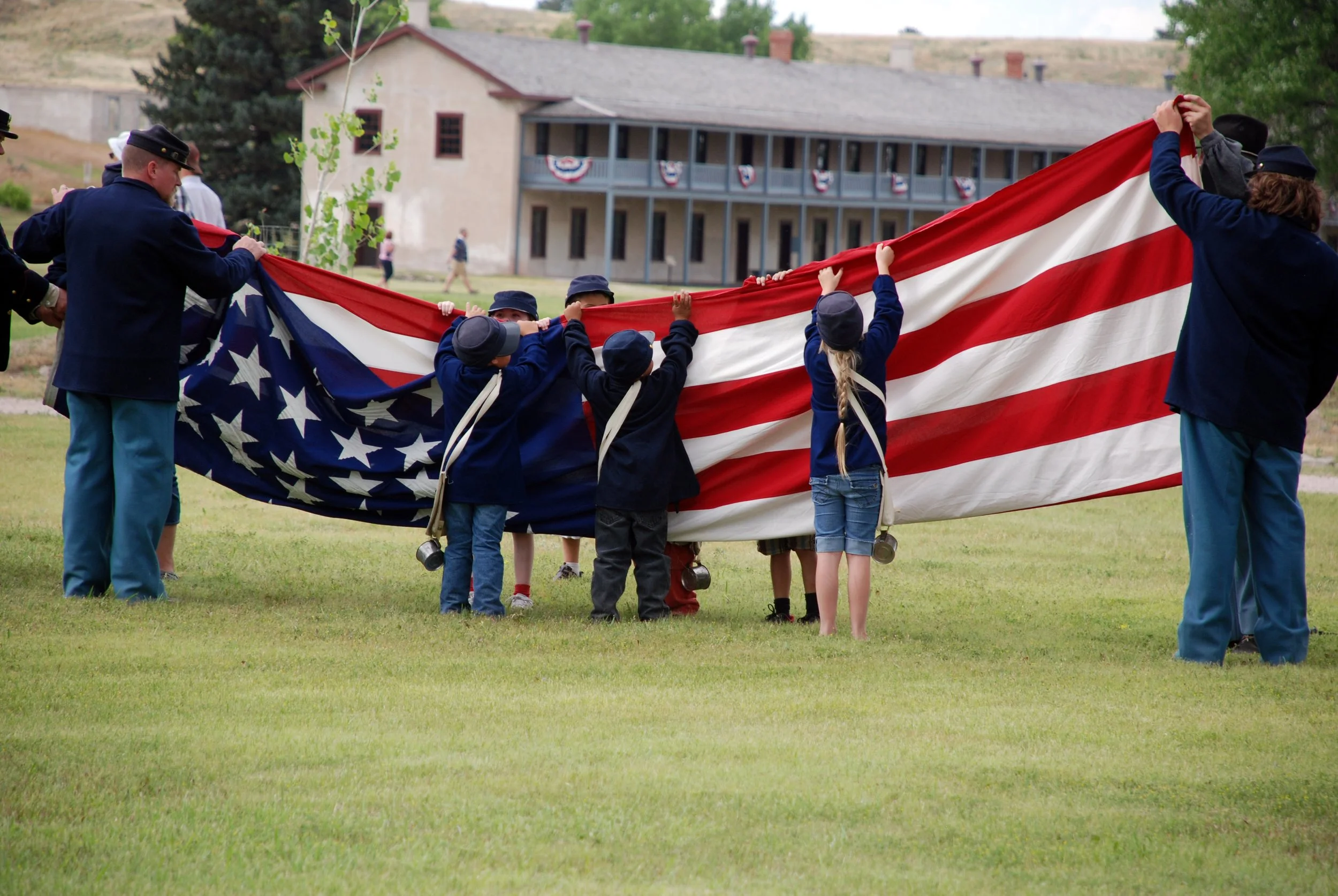 children dressed in Union uniforms help fold a US flag during a reenactment at Fort Laramie