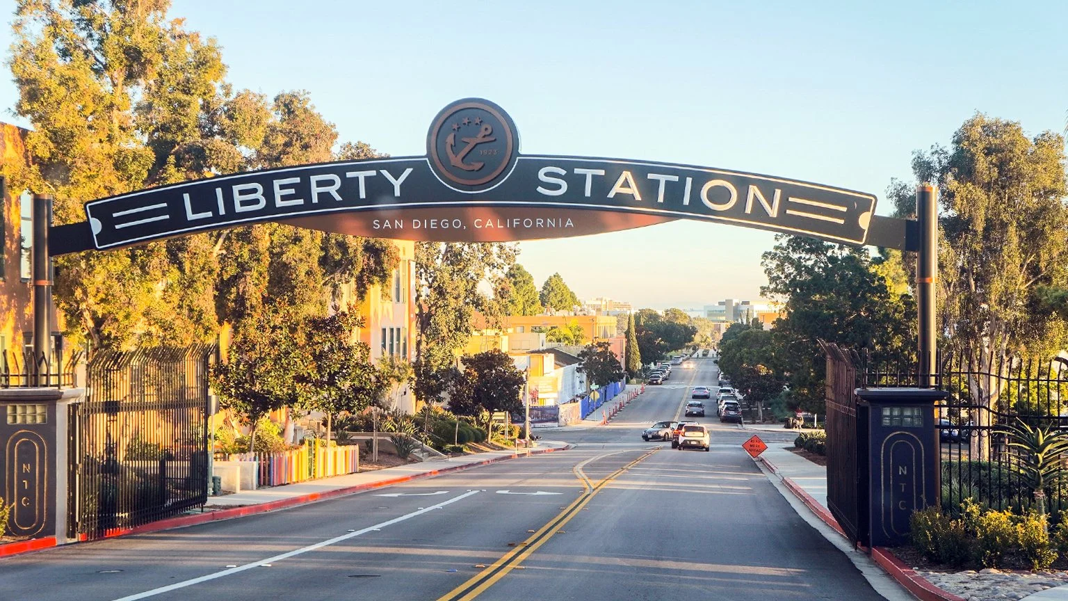 The Liberty Station sign arches over a road. It has an Anchor and three stars embossed on it. The sign reads: "Liberty Station, San Diego, California"