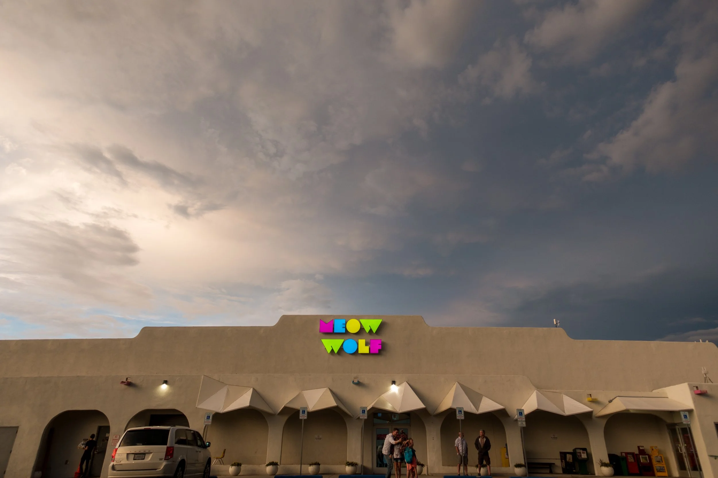 The white adobe entrance to Meow Wolf Santa Fe under a blue sky
