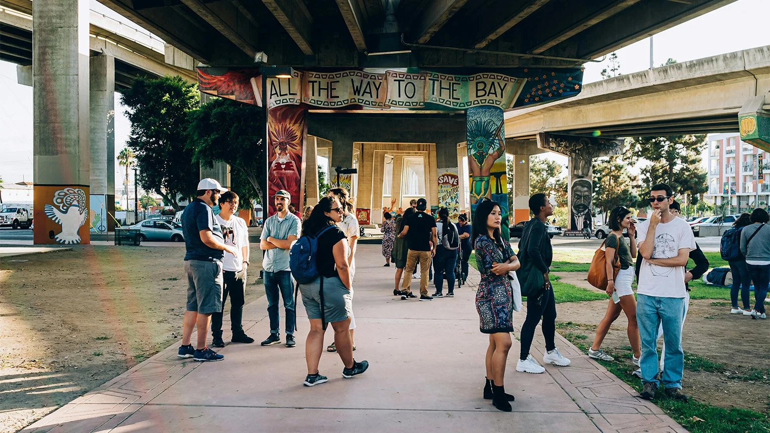 People stand around Chicano Park in Barrio Logan, San Diego, looking at graffiti under the freeways