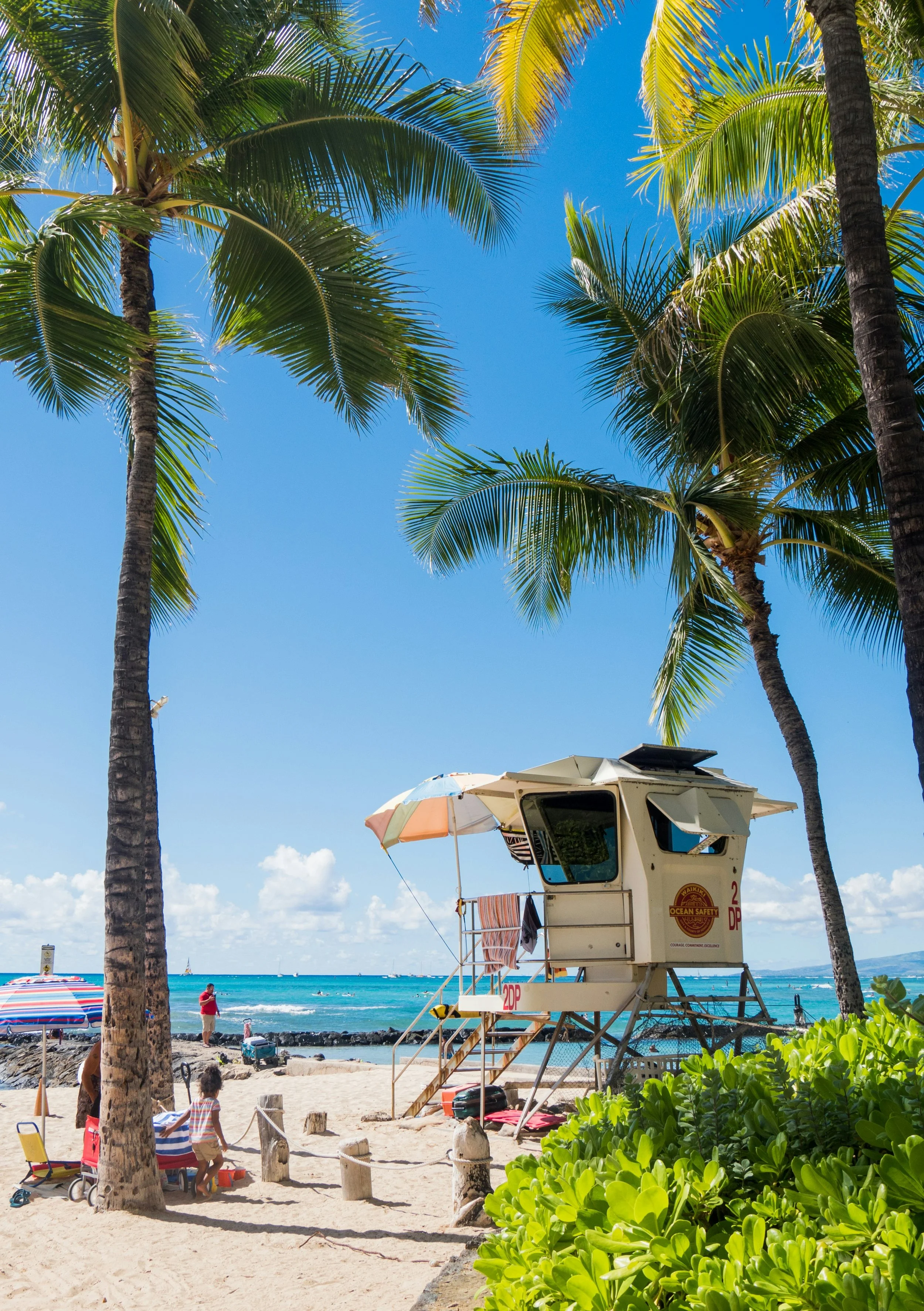 People relax and play under the palm trees and by a lifeguard station on Waikīkī Beach, Honolulu. Drives & Detours