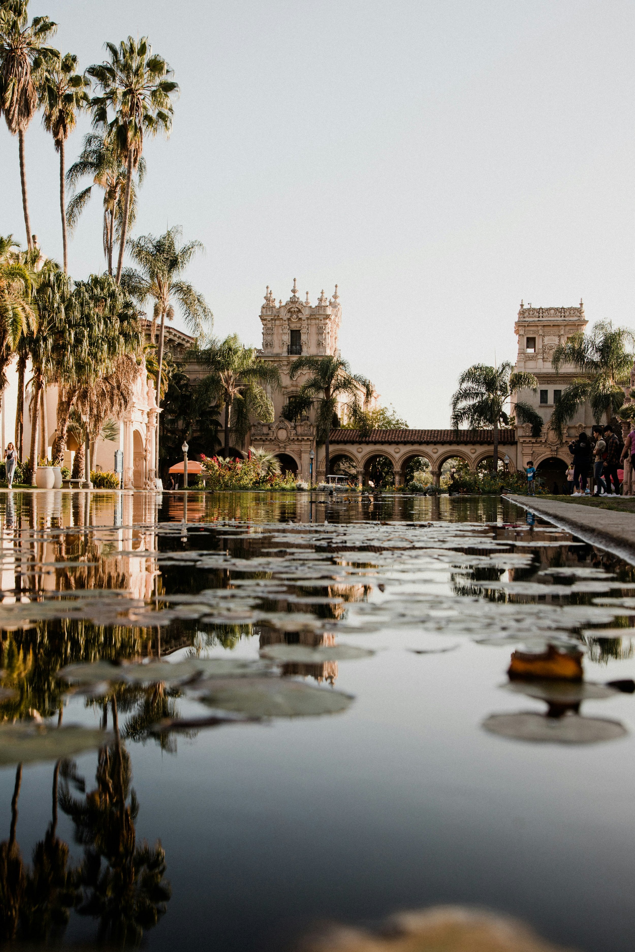 The pond and Spanish Revival style buildings are surrounded by palm trees in San Diego's Balboa Park on a sunny day