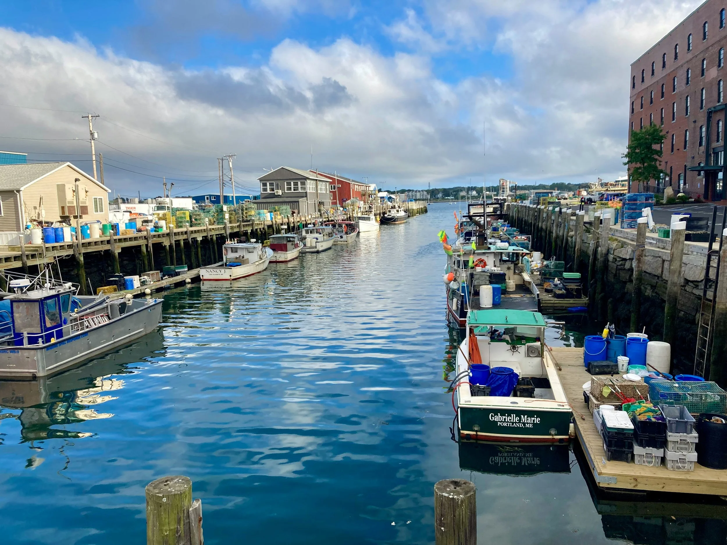 Small fishing boats float on the water in dock in Portland, Maine. The blue sky is reflected in the water