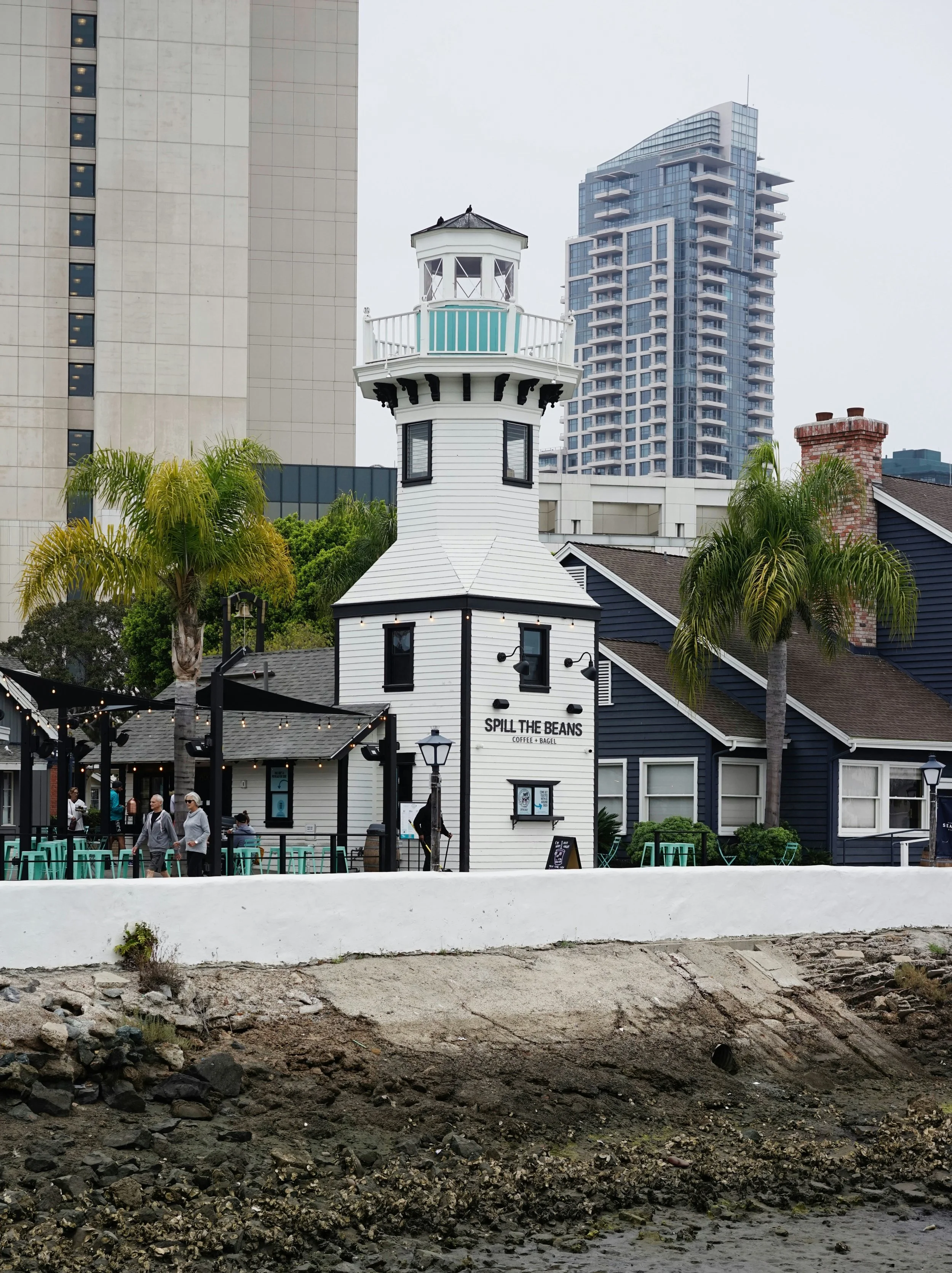 A small, white lighthouse with black detailing sits in Seaport Village near the San Diego Embarcadero. It has "Spill the Beans" written on it — the name of a local coffee shop