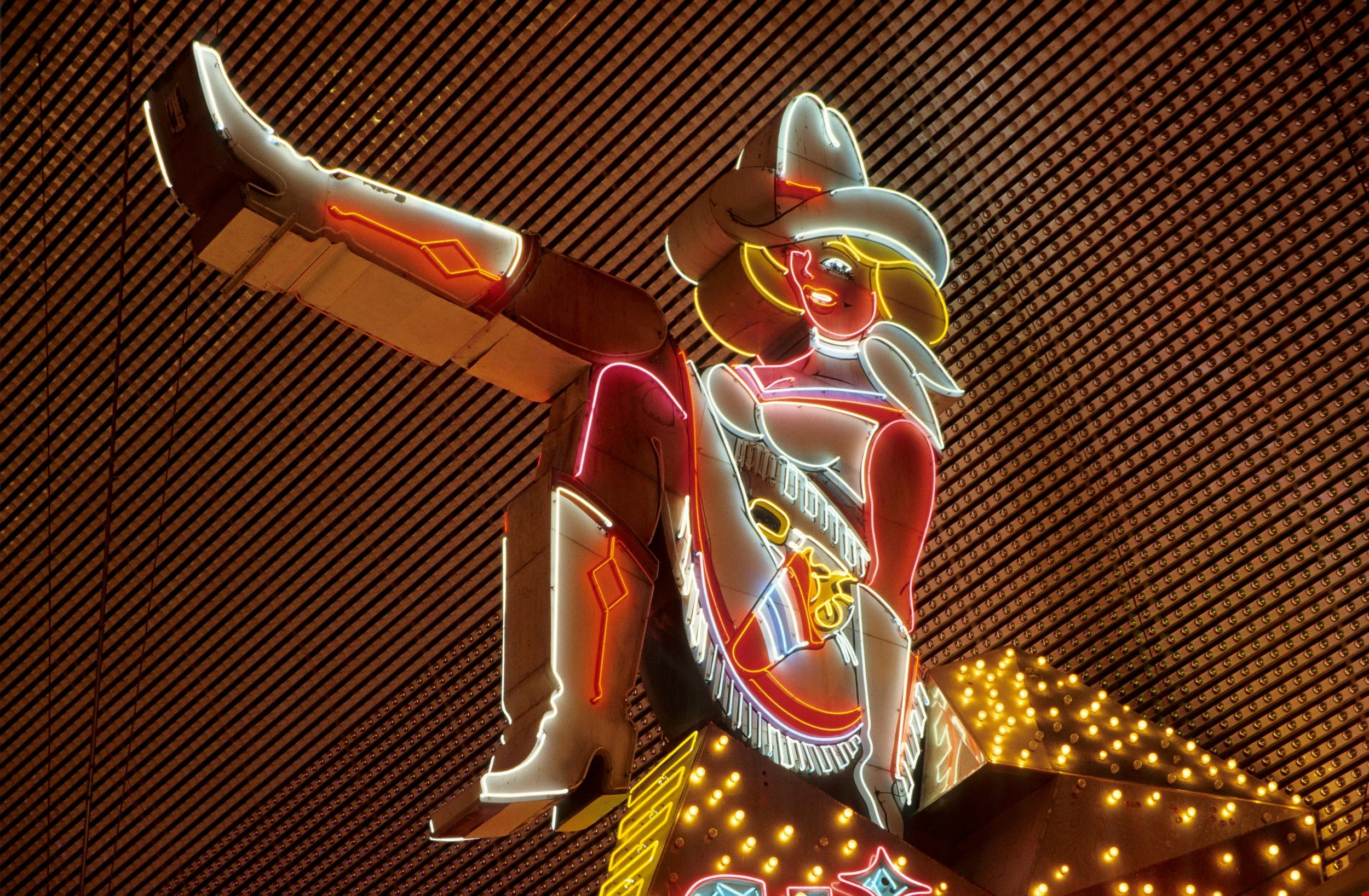 Vegas Vickie kicks her leg. She's a neon sign of a woman in a flirty position. Drives & Detours Las Vegas walking tour