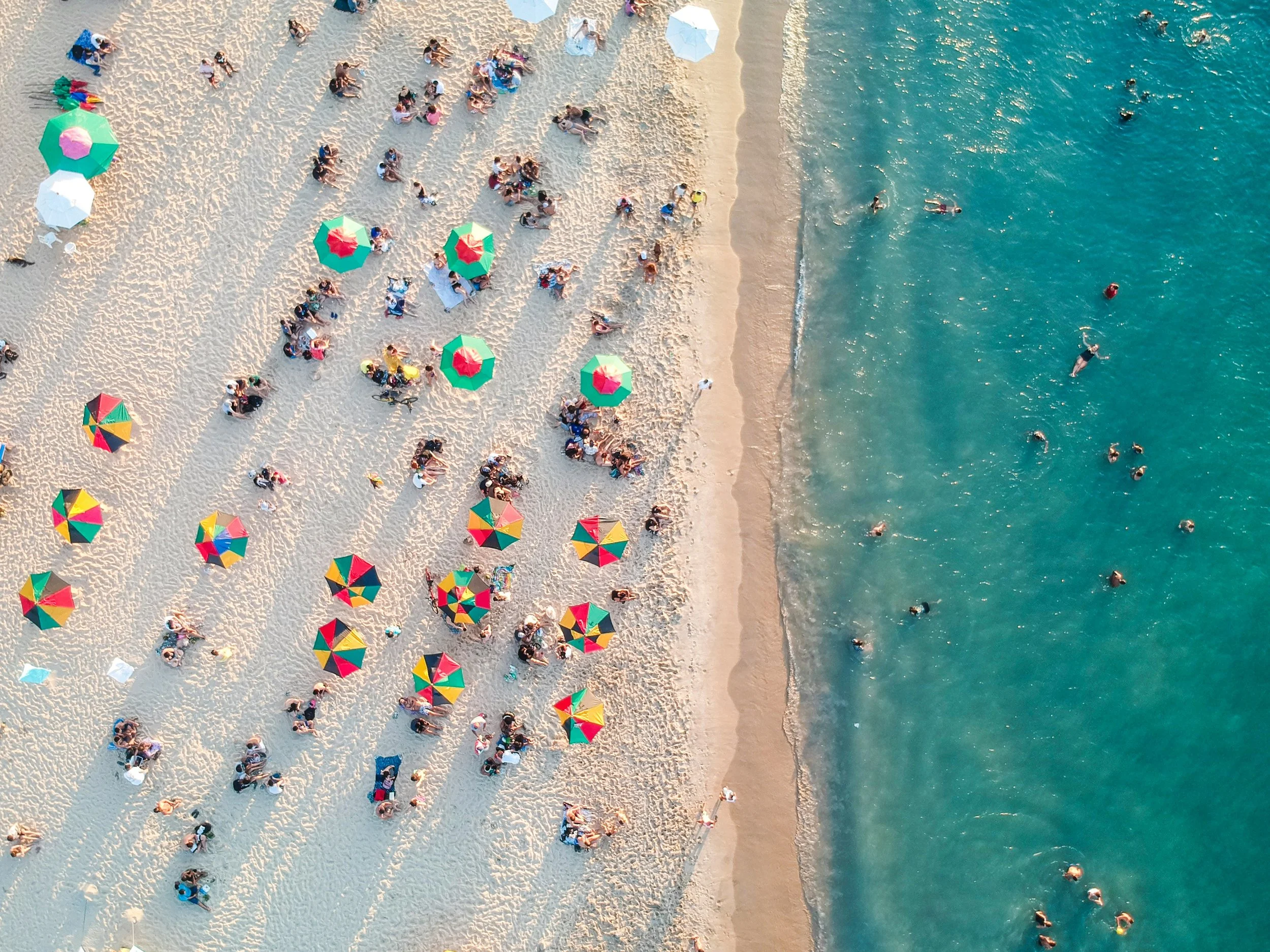 An aerial shot of Miami Beach. Parasols cover people on the sand while others play in water. Drives & Detours Miami local tips