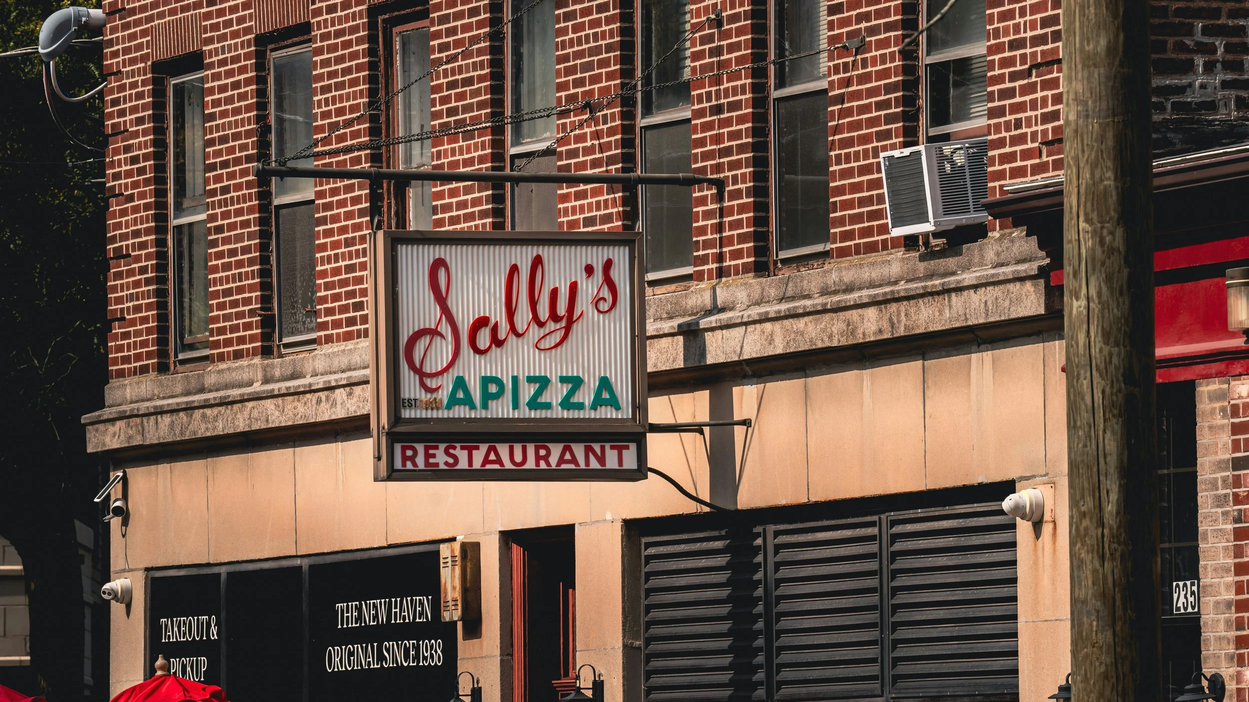 A sign outside a restaurant reads: Sallys Apizza Restaurant. Drives & Detours New Haven travel tips