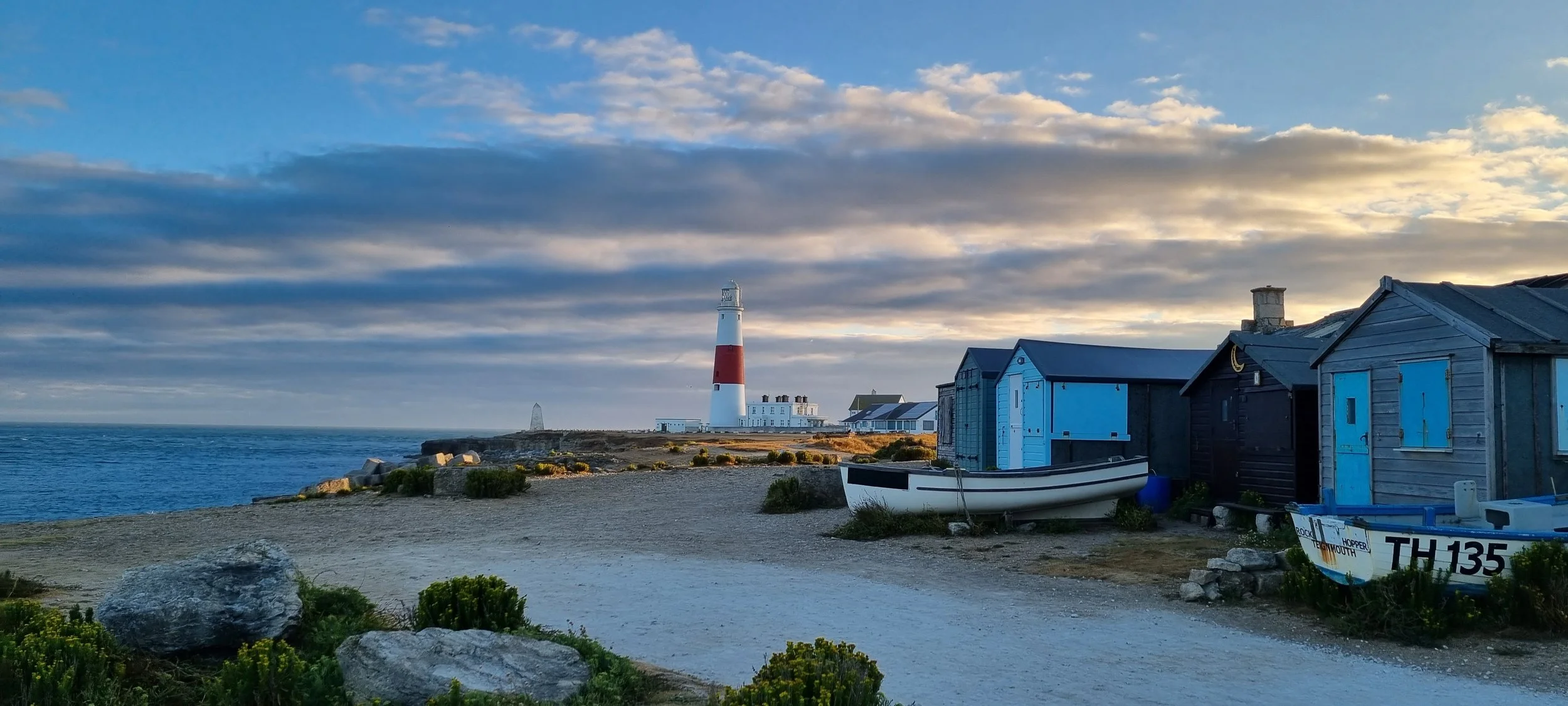 A tall lighthouse, beach shacks and wooden boats near Portland, Maine