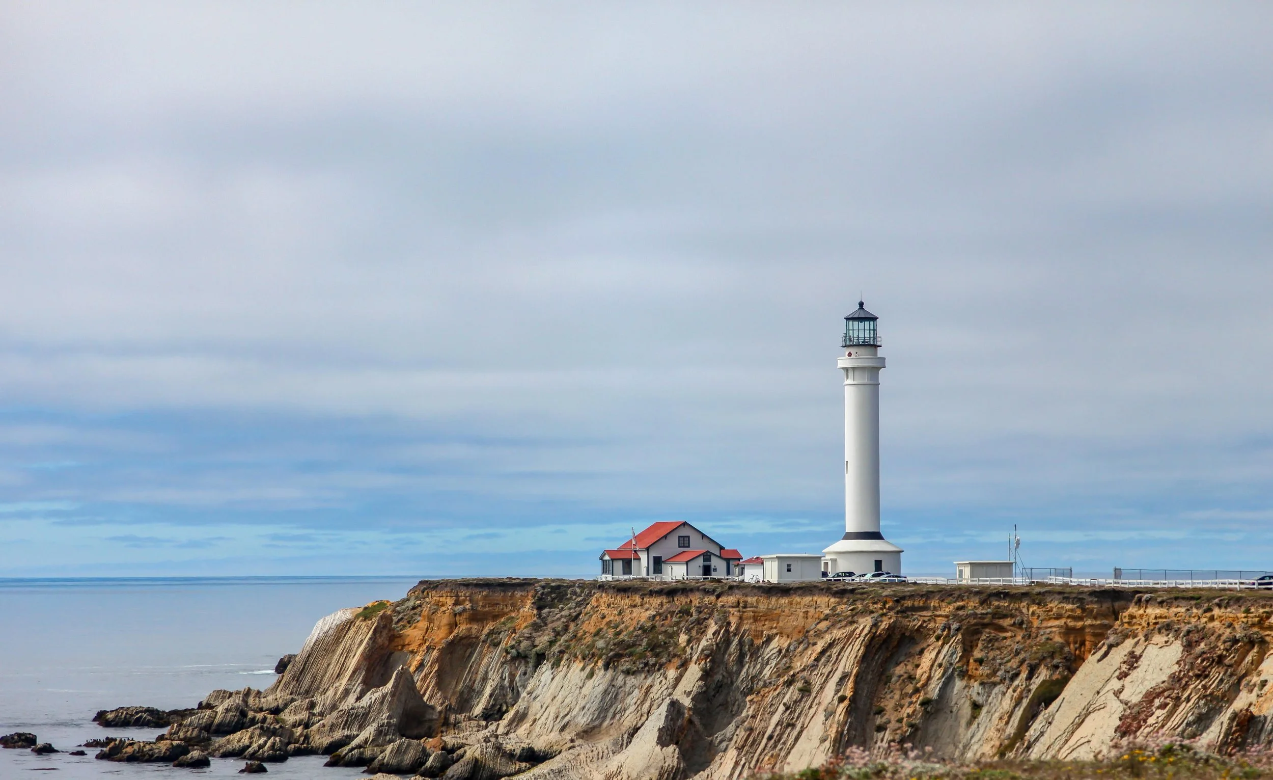 A tall, white lighthouse stands on top of a cliff near Mendocino, California.
