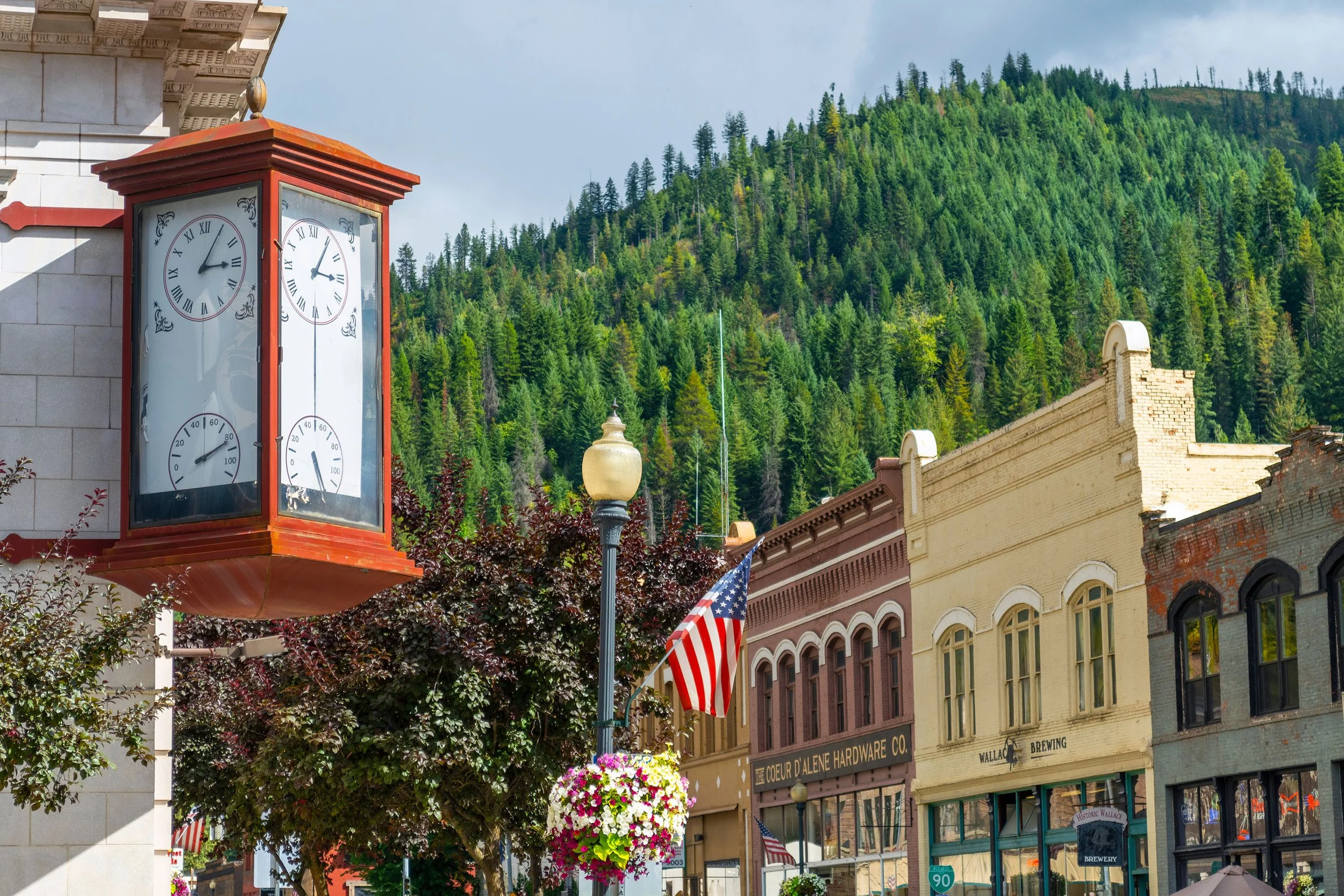 The historic clock at the center of Wallace, with pine covered hills in the background. Drives & Detours Wallace tour