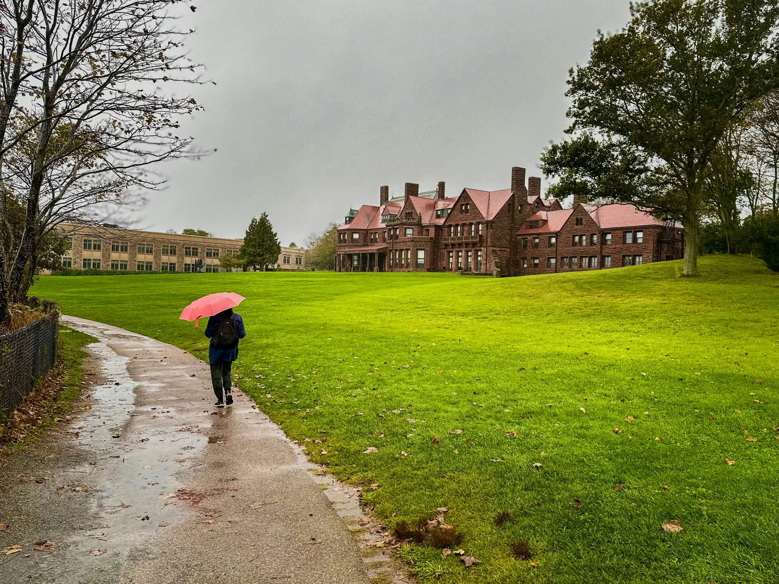 A woman walks past Salve Regina University under a pink umbrealla in the rain. Drives & Detours Newport Cliff Walk tips