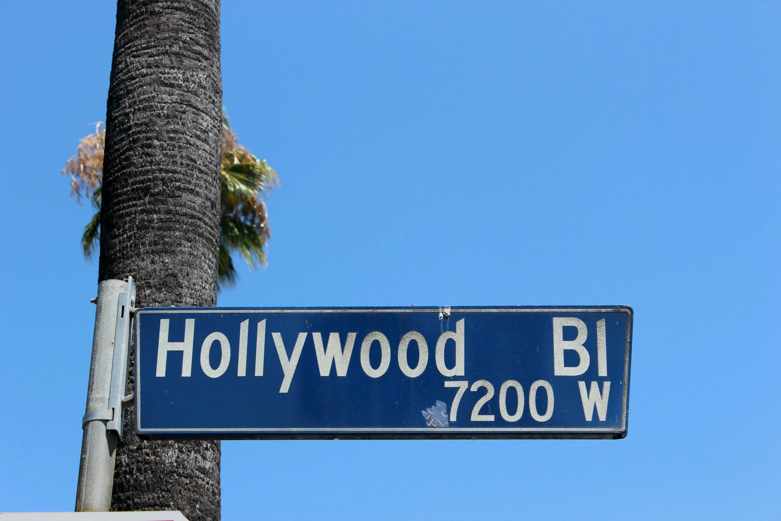 A close up of a street sign in Los Angeles with a blue sky behind it. Drives & Detours Hollywood Audio Tour