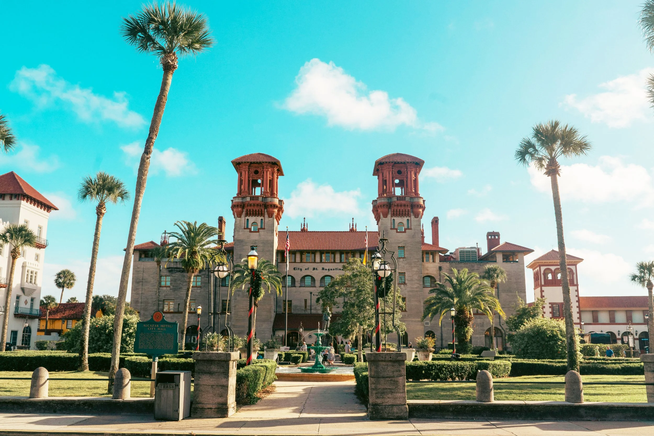 The Lightner Museum in St. Augustine used to be the Hotel Alcazar, which dates to the Gilded Age. The buildings two towers stand over a huge edifice, with manicured gardens in front and a bright blue sky behind