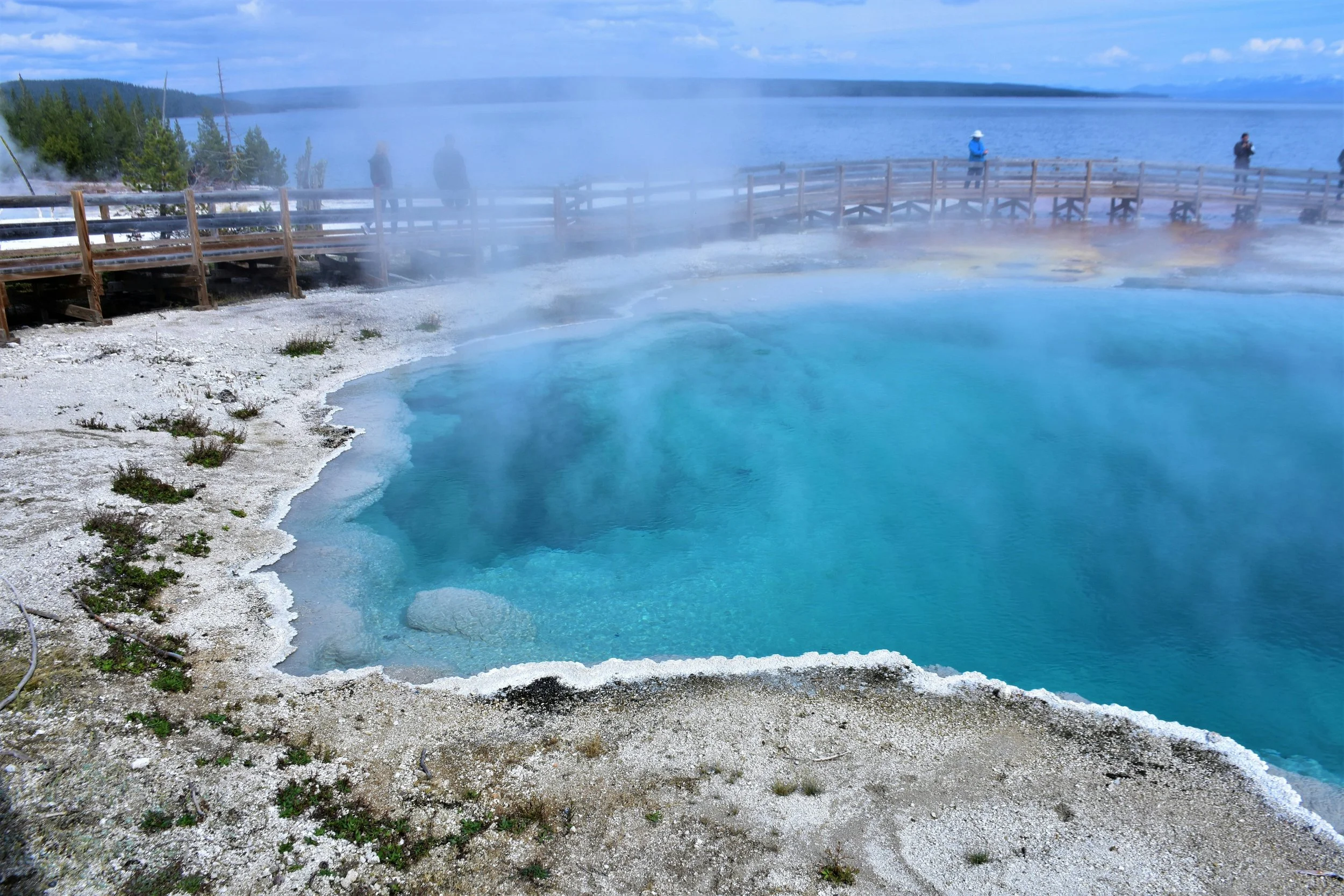 People walk around a hot spring in the West Thumb Geyser Basin with a huge lake in the background. Drives & Detours best things to do in Yellowstone