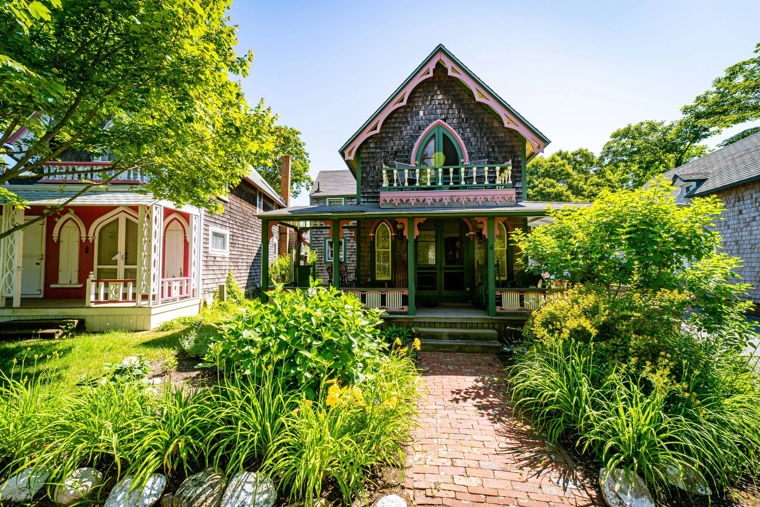 One of the Gingerbread Cottages in Oak Bluffs, Martha's Vineyard. Its beautifully decorated with pink and green details, and has a small garden overflowing with plants