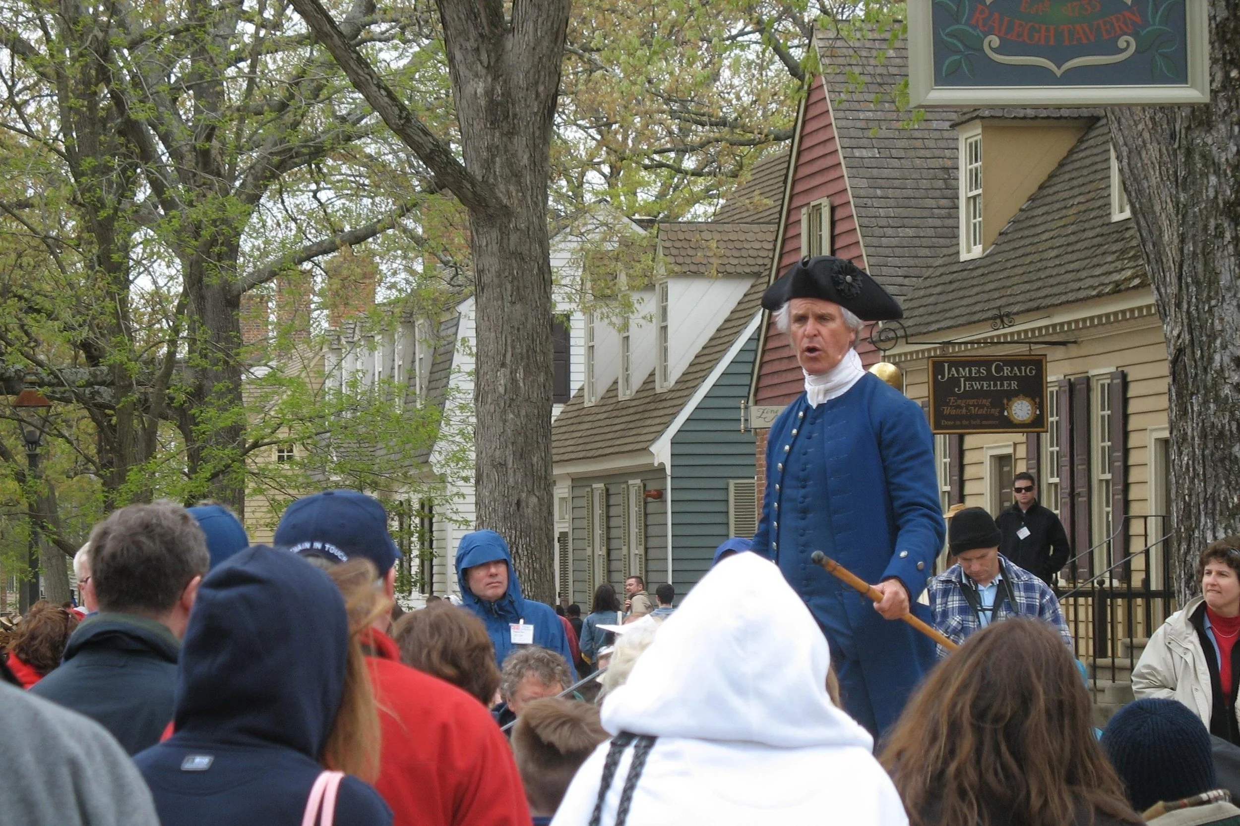 A town crier speaks to a crowd in Colonial Williamsburg. He's in an old three-pointed hat, with a blue suit from colonial times