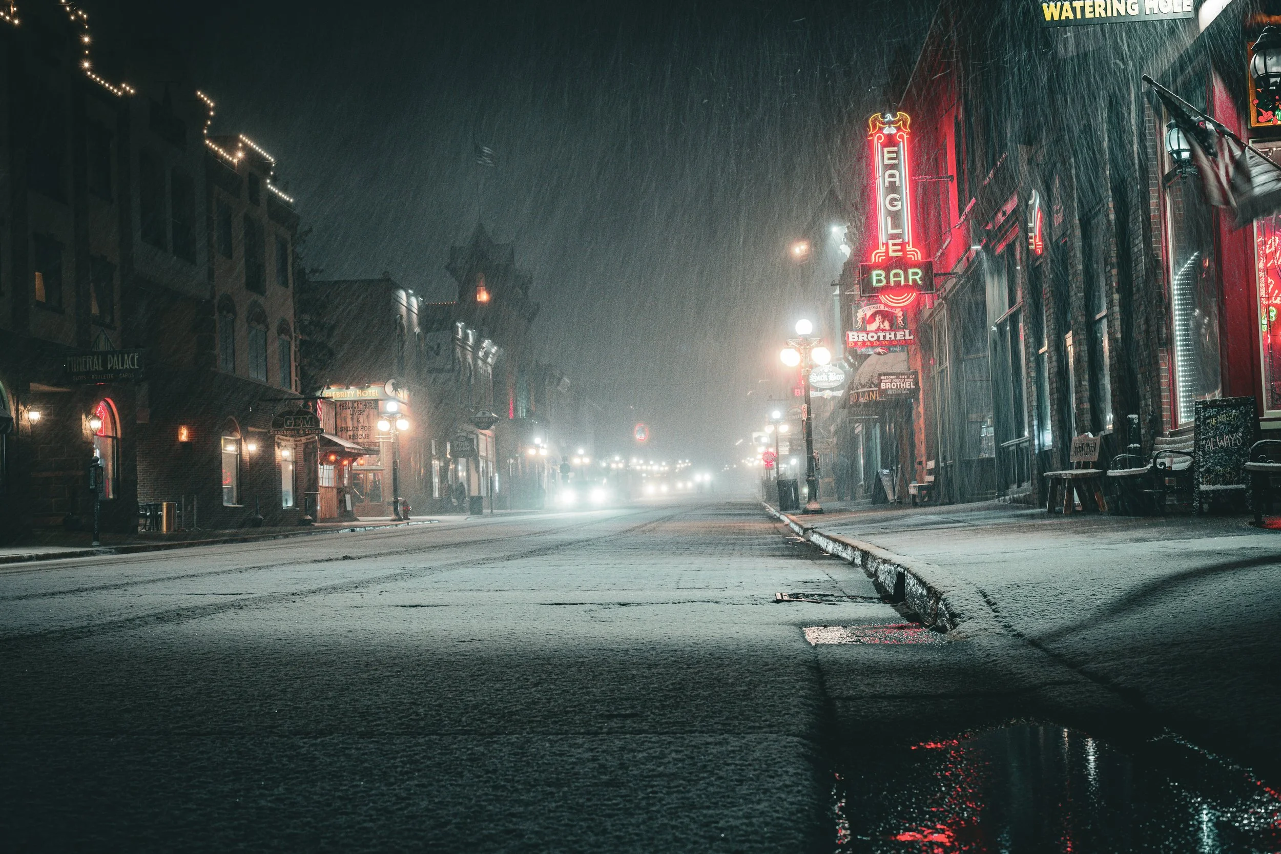 Snow falls heavily at night through the lights of a main street in a wild west town in South Dakota. Drives & Detours Deadwood tour