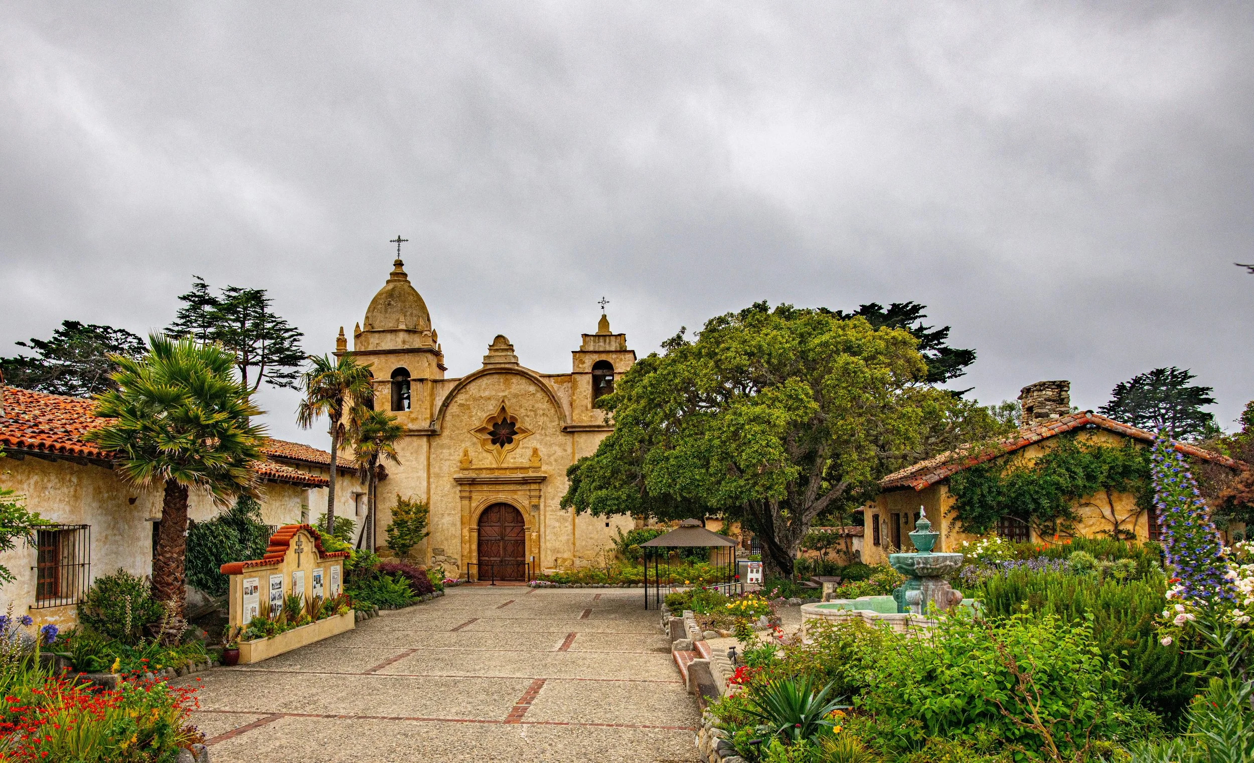 A postcard-like view from the center of Carmel-by-the-Sea. A small church is surrounded by cottages, fountains and flowers