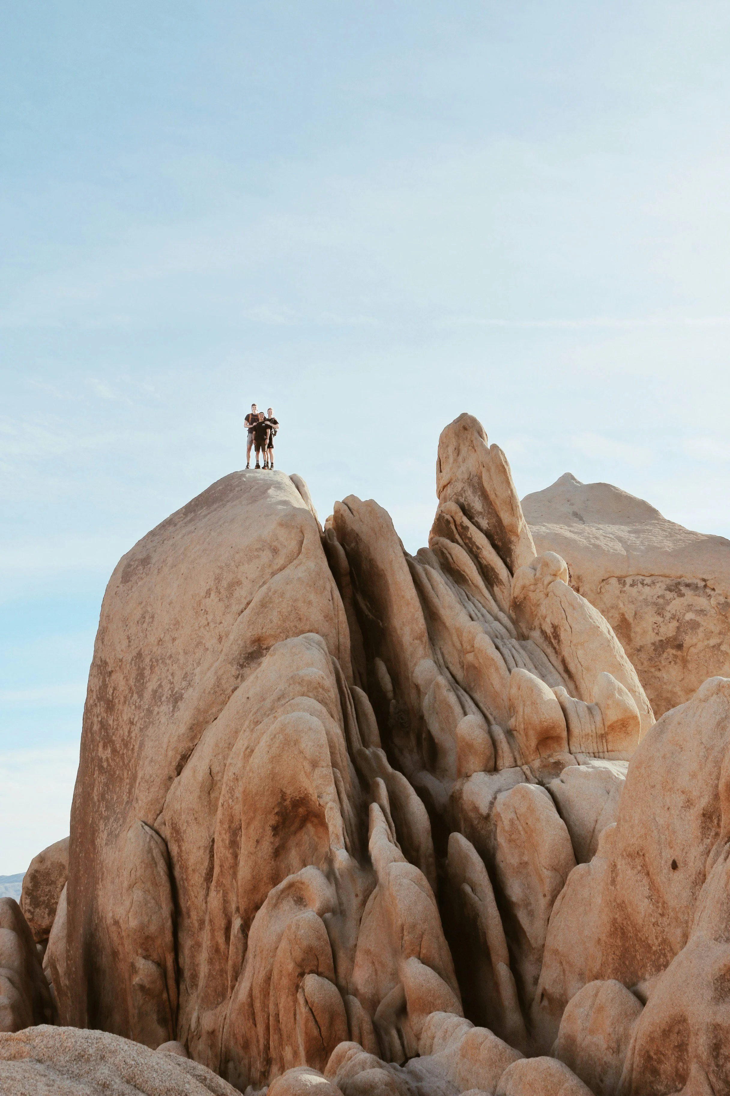 Three people stand on top of a beautiful rock formation, smooth from weathering. The people must be 100 feet above the ground