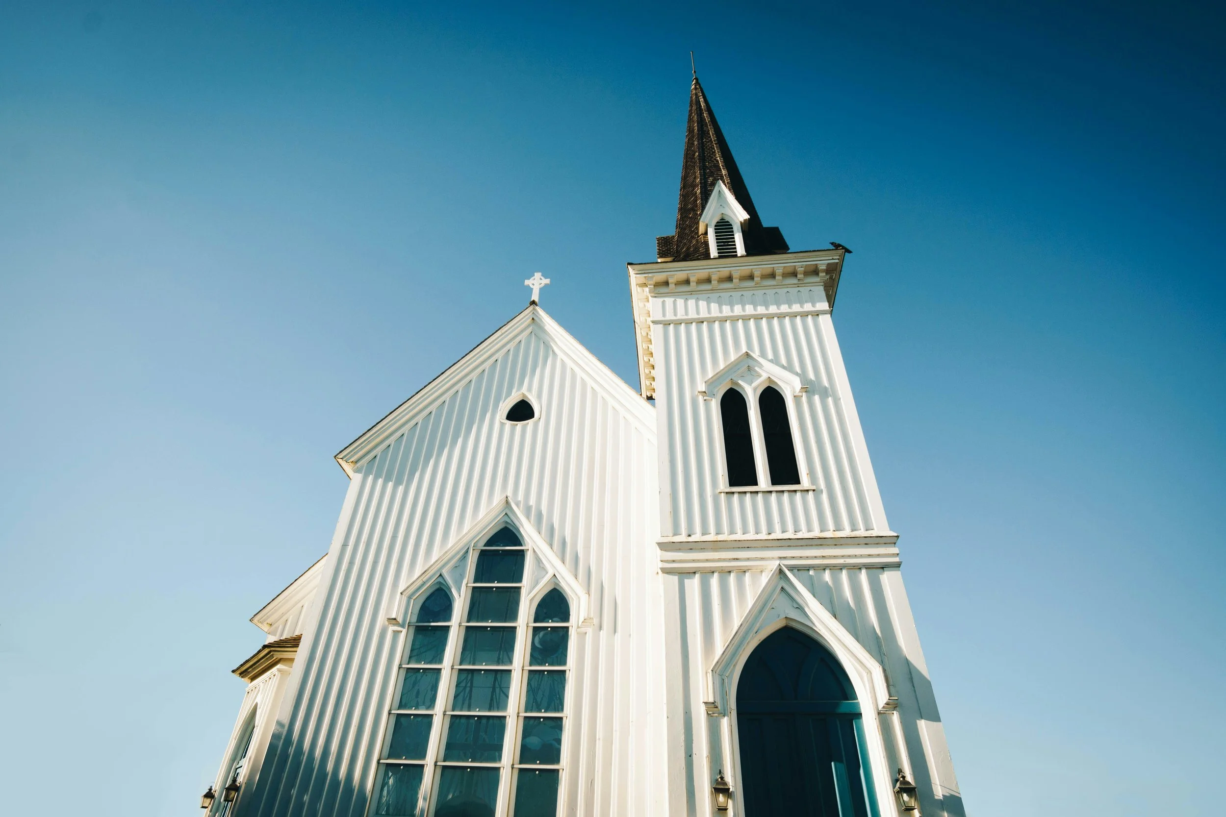 A white wooden church against a blue sky. It's not large, but the angle makes it look towering. Drives & Detours Mendocino walking tour