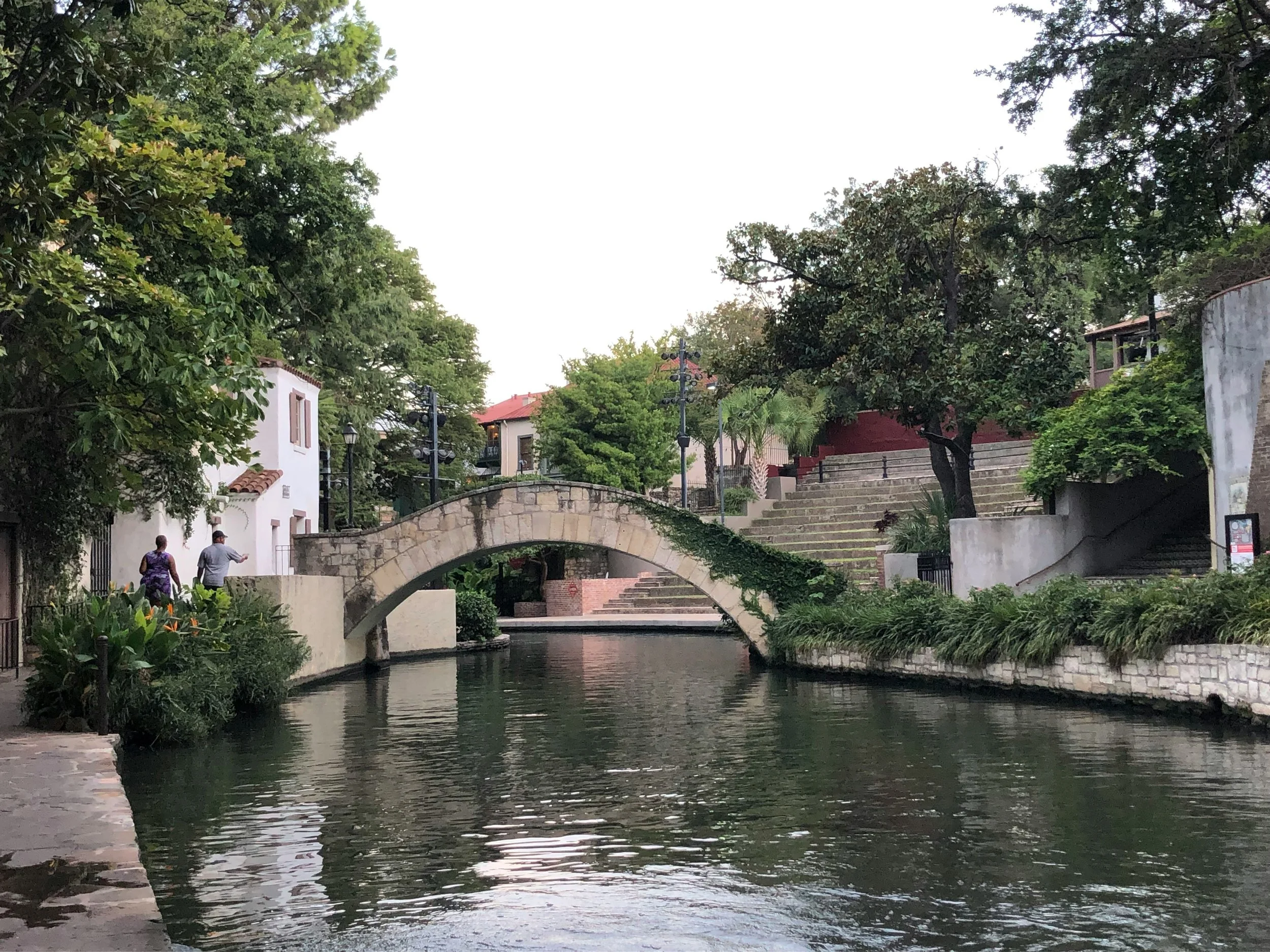 An old stone bridge covers the San Antonio river. People walk along the banks Drives & Detours. Best places to eat in San Antonio