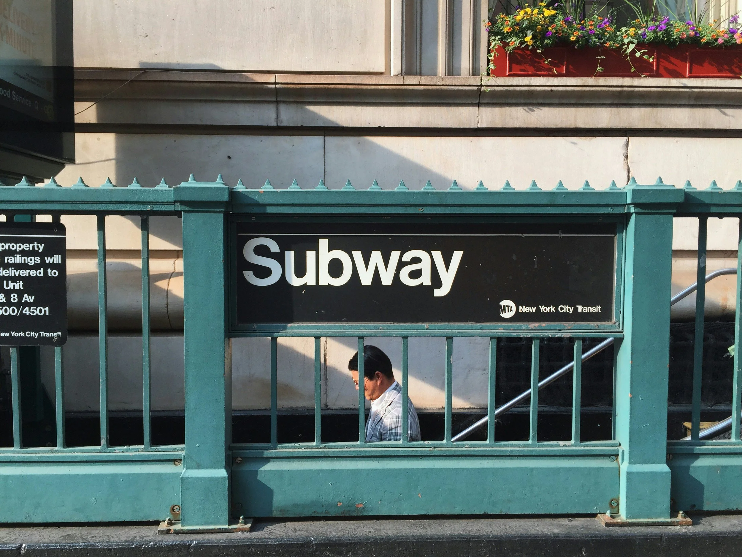 A man walks down some steps behind green railings. A sign reads: Subway. Drives & Detours NYC local tips