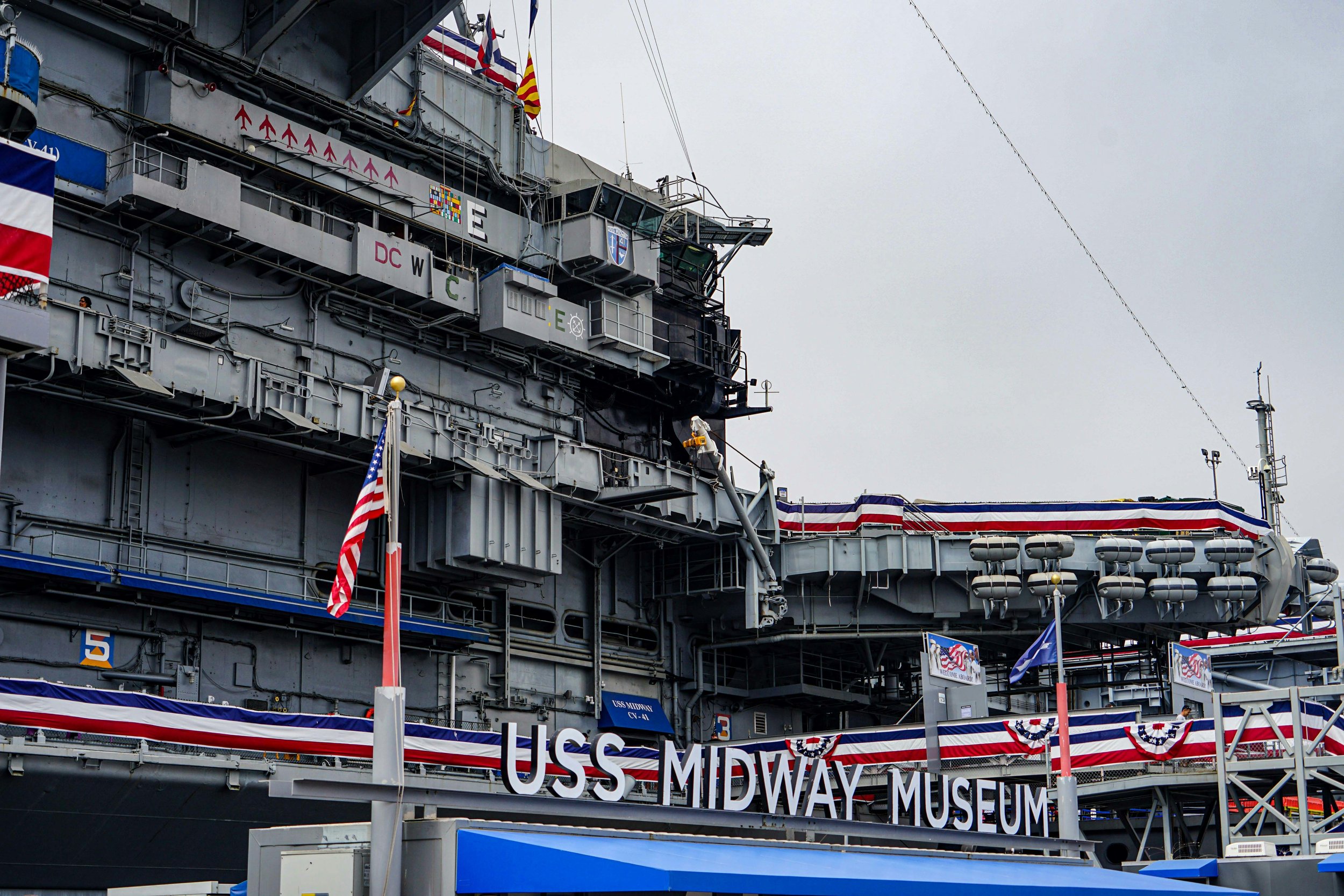 A deatil of the decks of a ship, decked out in red, white and blue. The words USS Midway Musuem are written on a sign