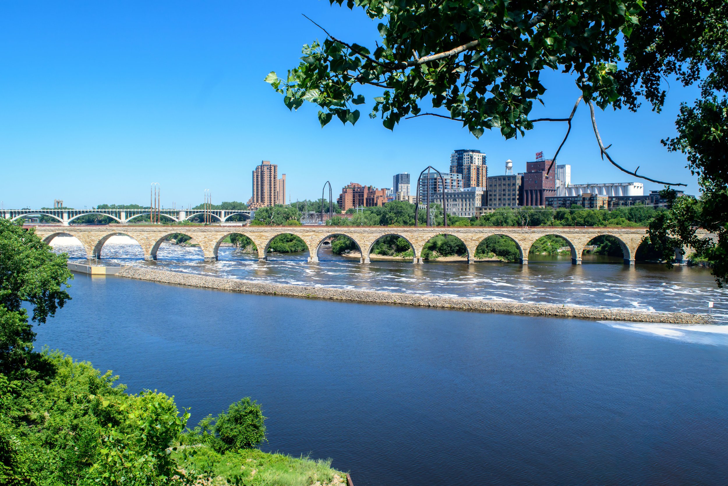 The Stone Arch Bridge crosses the Mississippi River under a bright blue sky. Drives & Detours Minneapolis self-guided tour