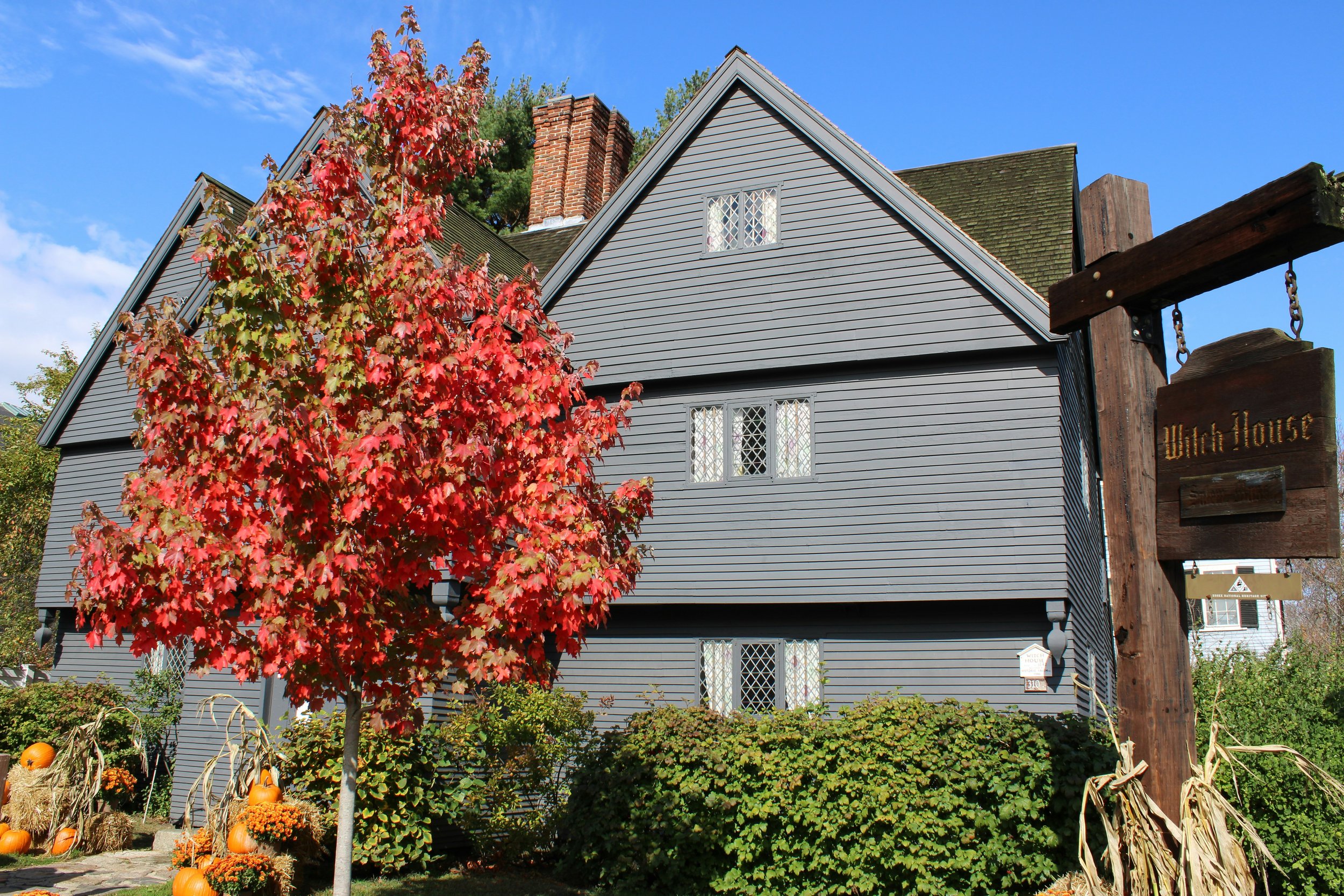 The Witch House at Salem, Massachusetts, is a large black, wooden building with small windows. A tree with red leaves stands outside. Drives & Detours Salem self-guided tour