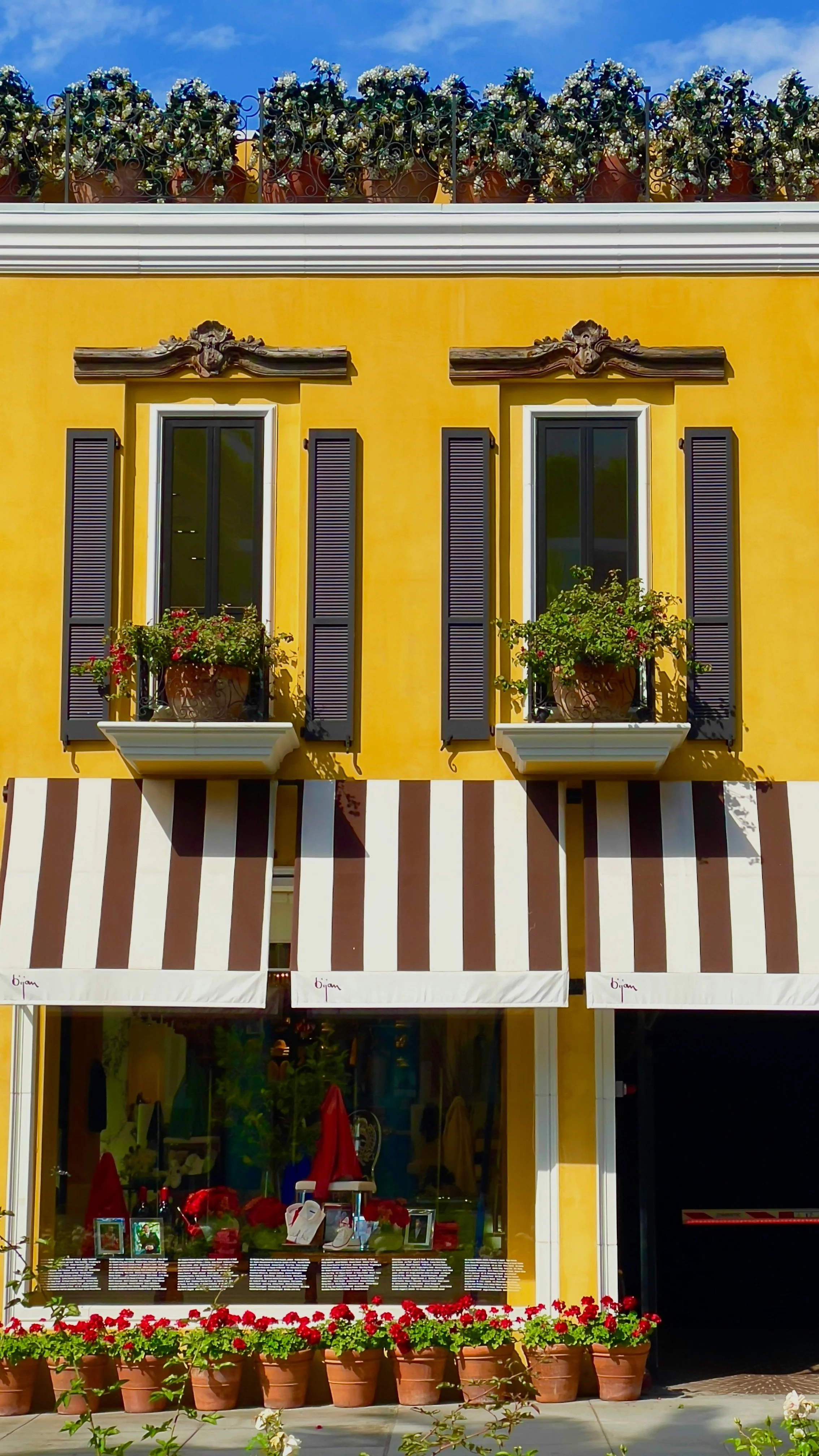 A yellow shop in Beverly Hills, Los Angeles. The shop window is lined with roses and the second floor windows have small balconies with big plant pots