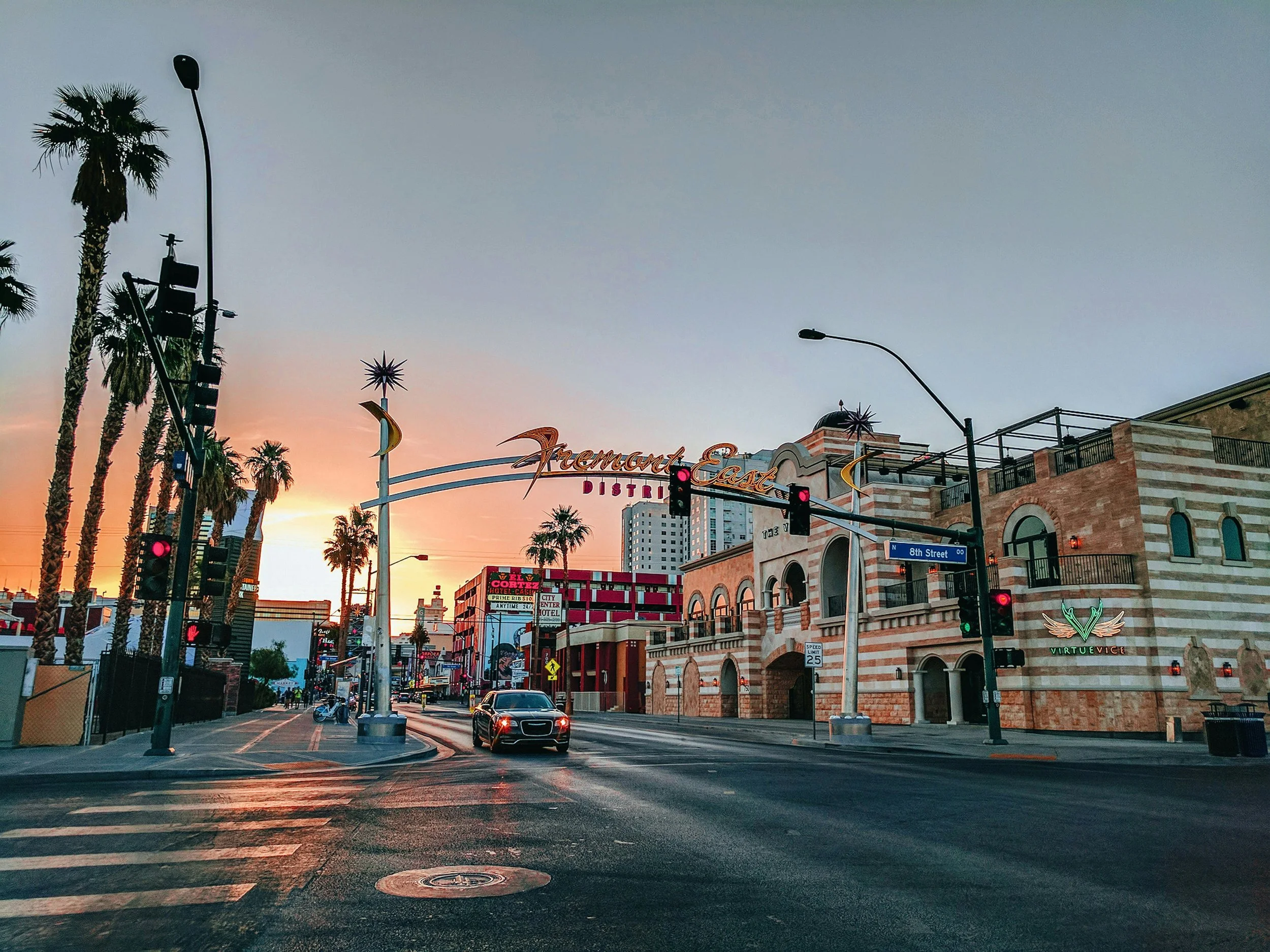 The entrance to Fremont Street at sunset. A sign crosses the street which is lined with palm trees.