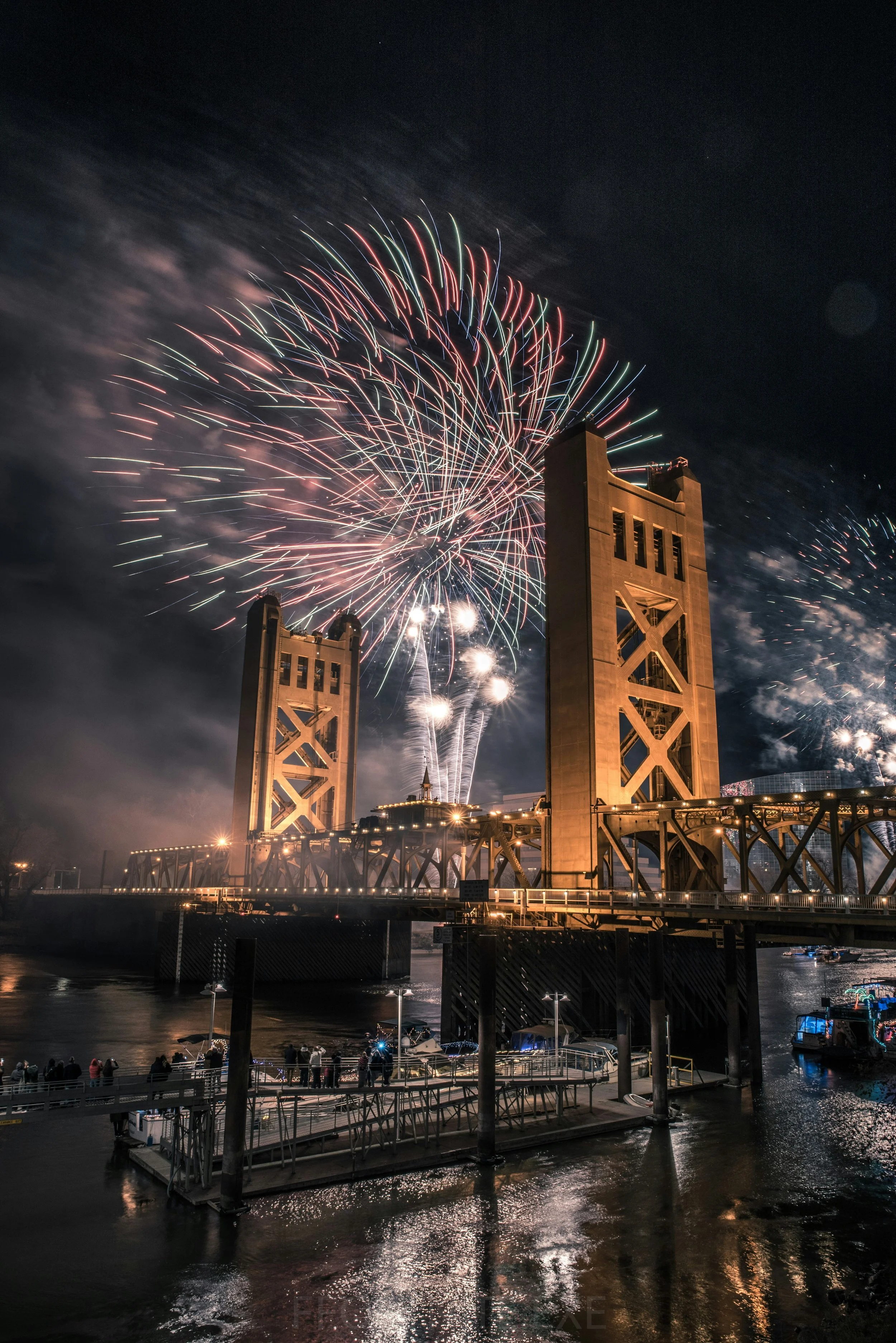 Fireworks burst over the golden Tower Bridge over the river by Old Sacramento