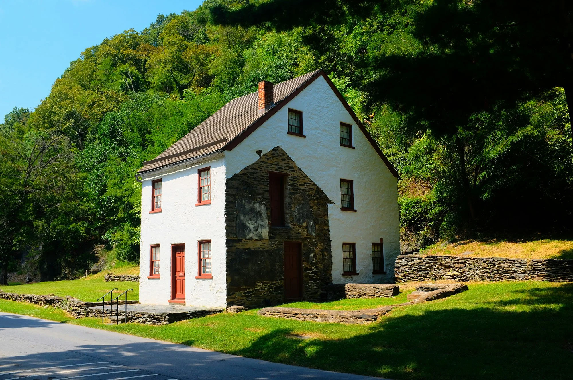An old white house in Harpers Ferry. It has red doors and window farmes, and you can see where an outhouse was attached