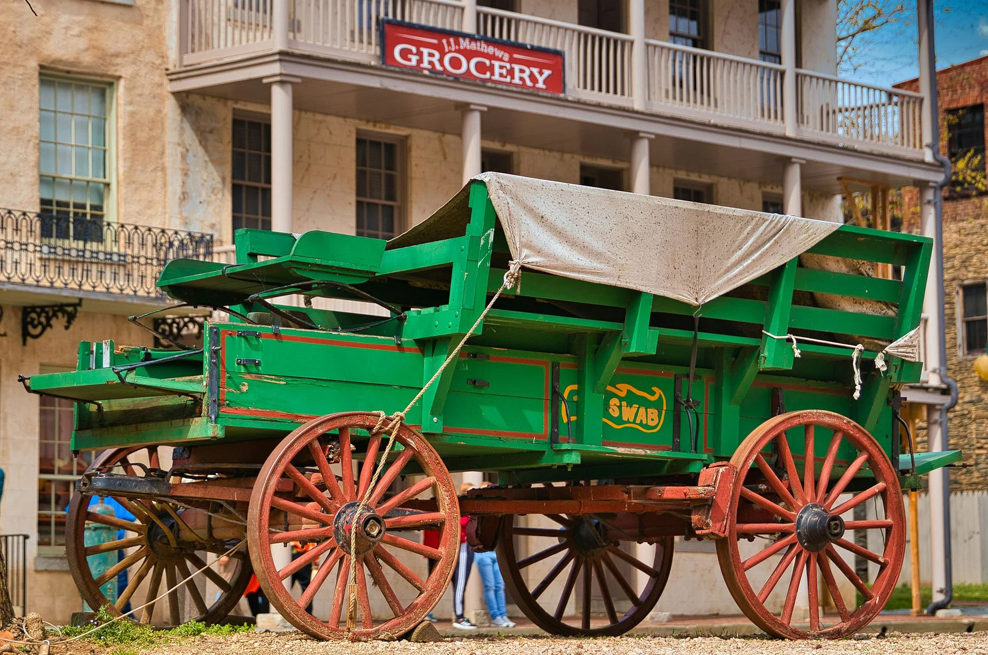 A green, vintage wagon with red wheels sits in front of a wild west grocery store. Drives & Detours Harpers Ferry self-guided tour