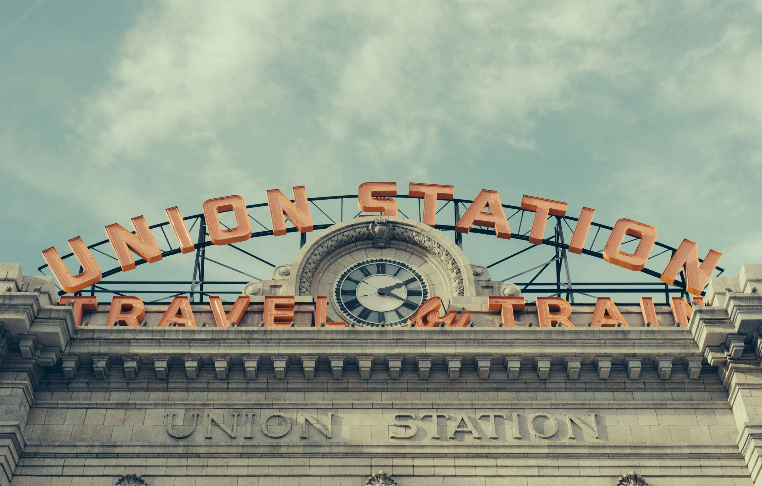 The sign of Denver Union Station surrounds a clock. It also reads: Travel by Train