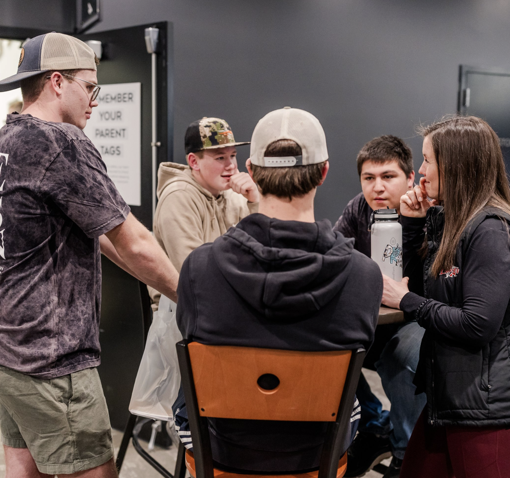 Group of five young people sitting and standing around a table, engaging in conversation.