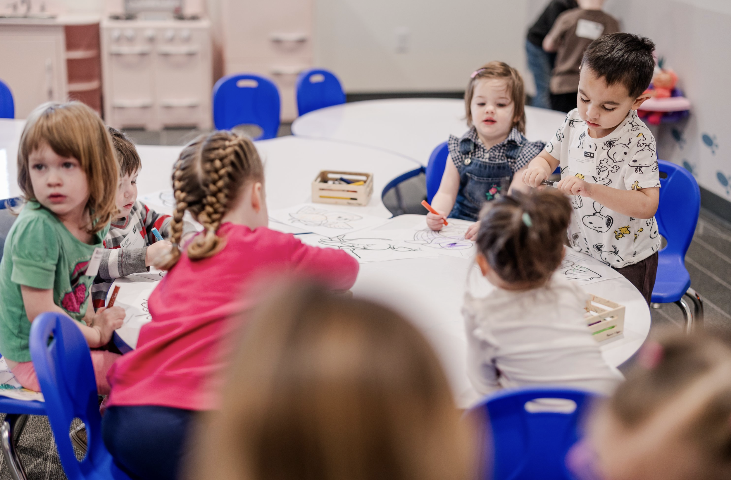 Children sitting around a table coloring with markers in a classroom or playroom.