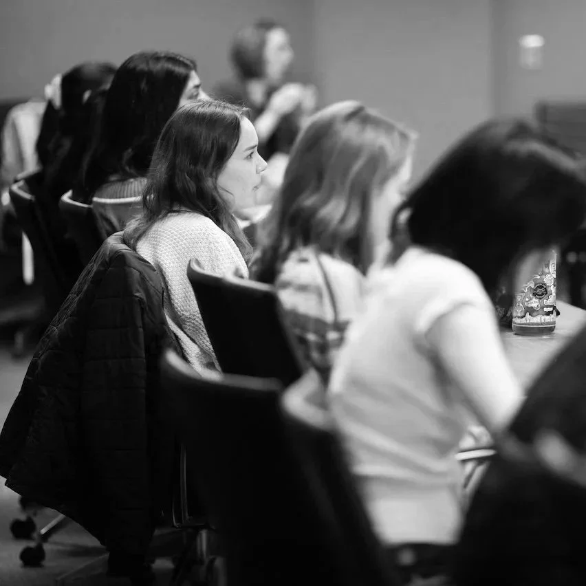 A group of young women at UW-Madison sitting in a classroom or conference room, attentively listening to a presentation or lecture.