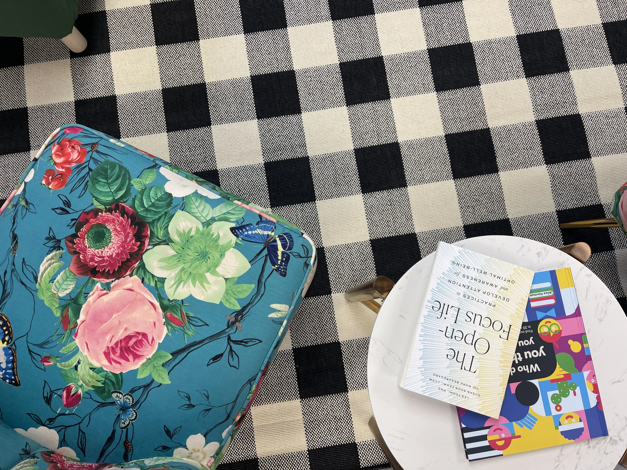 A tabletop with a black and white checkered rug, a colorful floral backpack, a white collapsible bowl with pamphlets, and colorful children's books. Windsor Worx Coworking